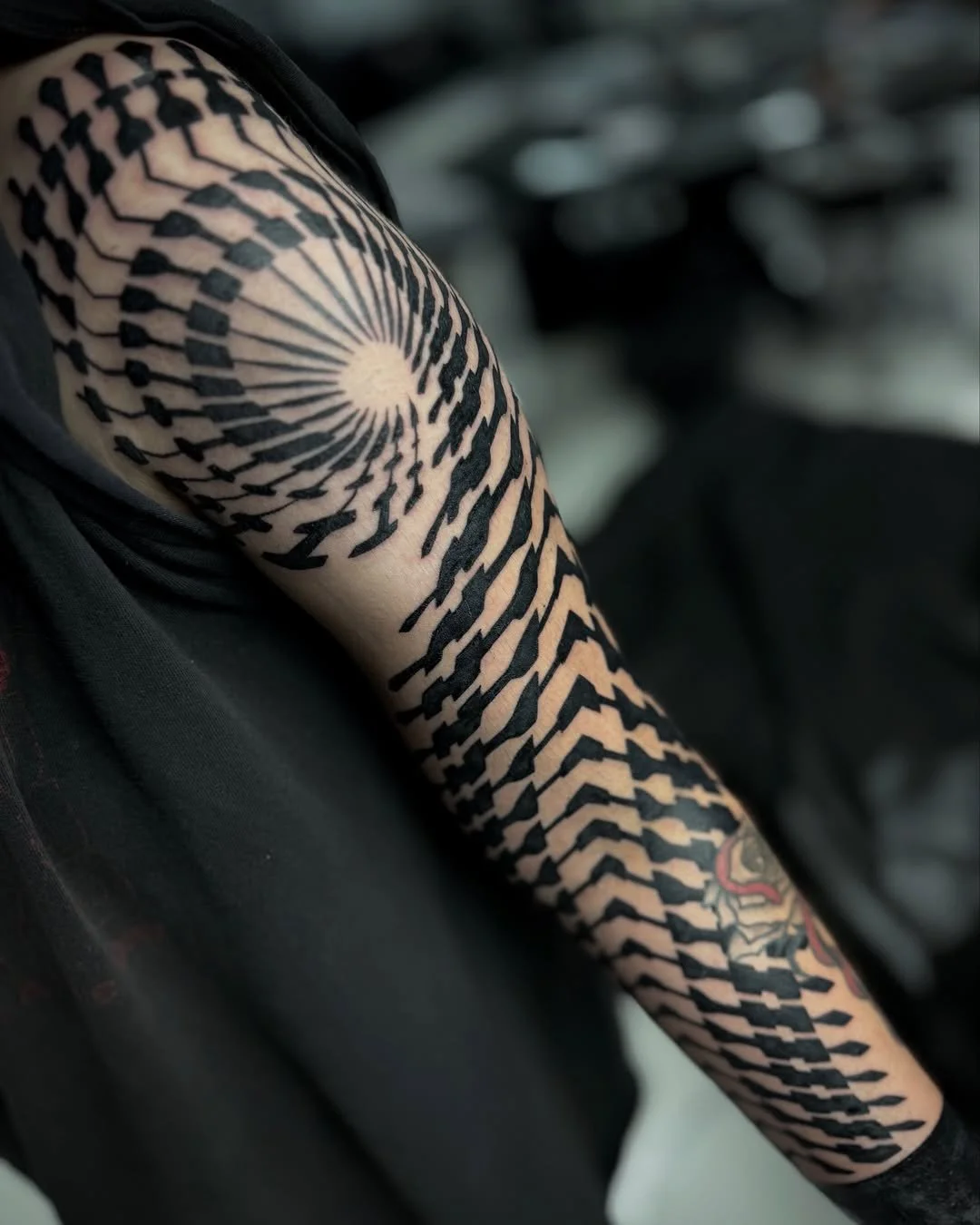 Tattoo of a spiral pattern with geometric black lines on a person's upper arm.