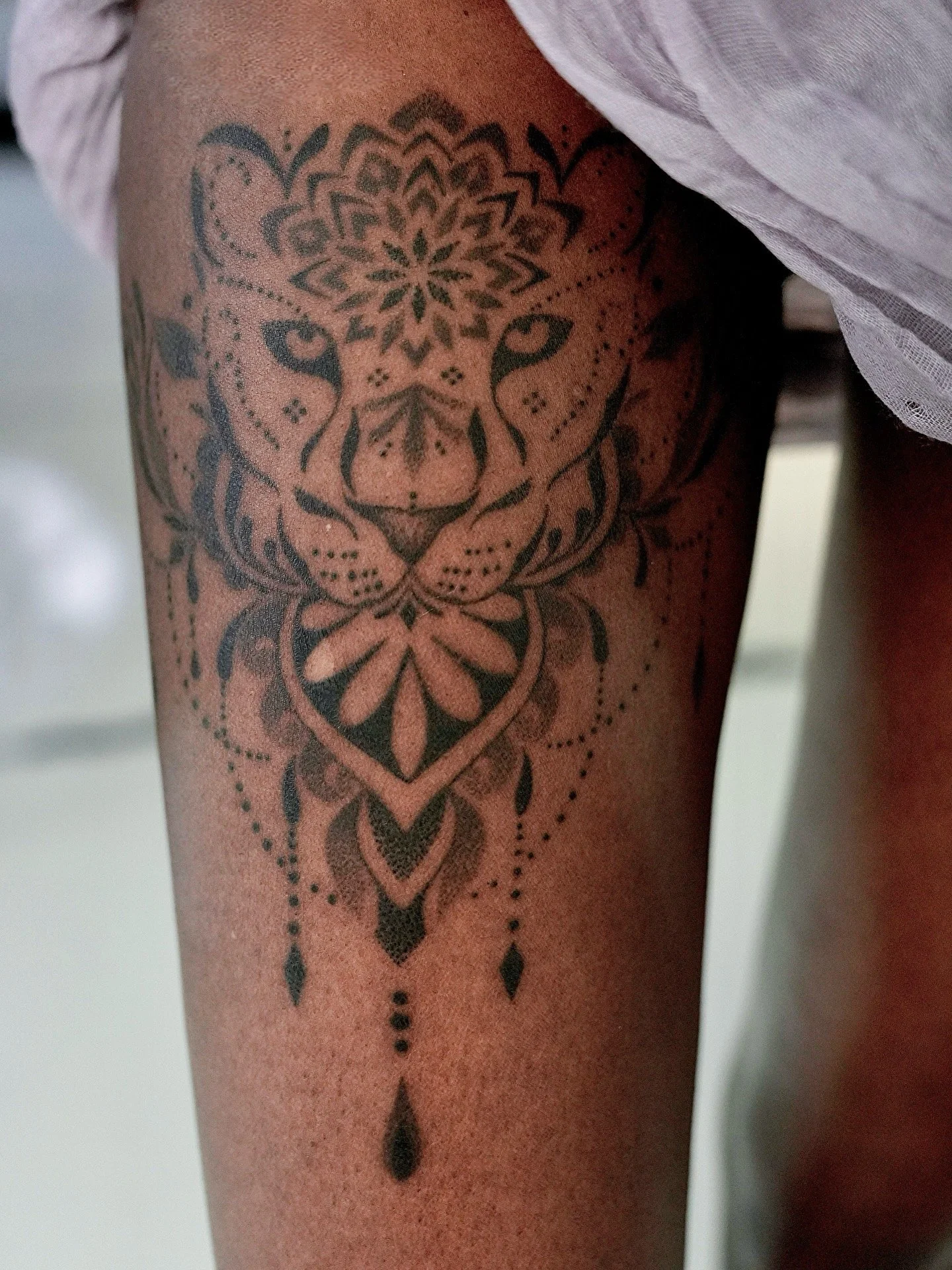 Tattoo of a stylized lion's face with intricate patterns and geometric designs on a person's forearm.