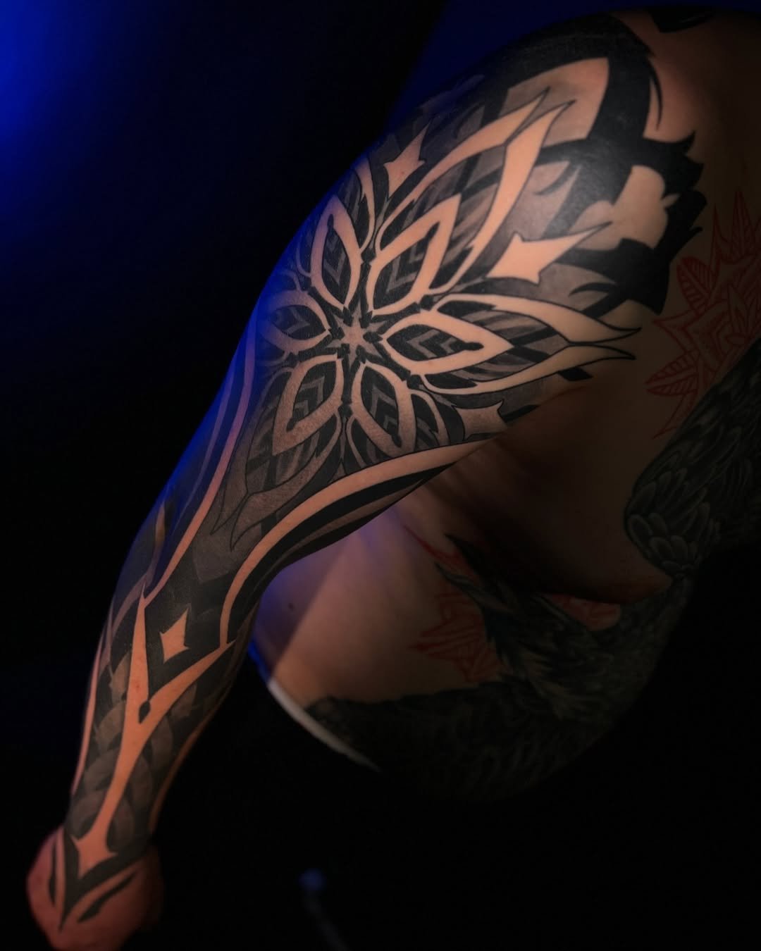 Close-up of a person's shoulder and arm with a large, intricate black tribal tattoo design on the skin.