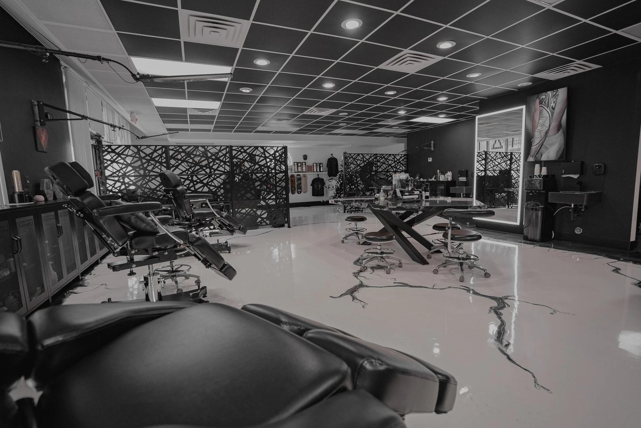 Interior of a modern tattoo parlor with tattoo chairs, a bar-style seating area, and decorative black wall panels.