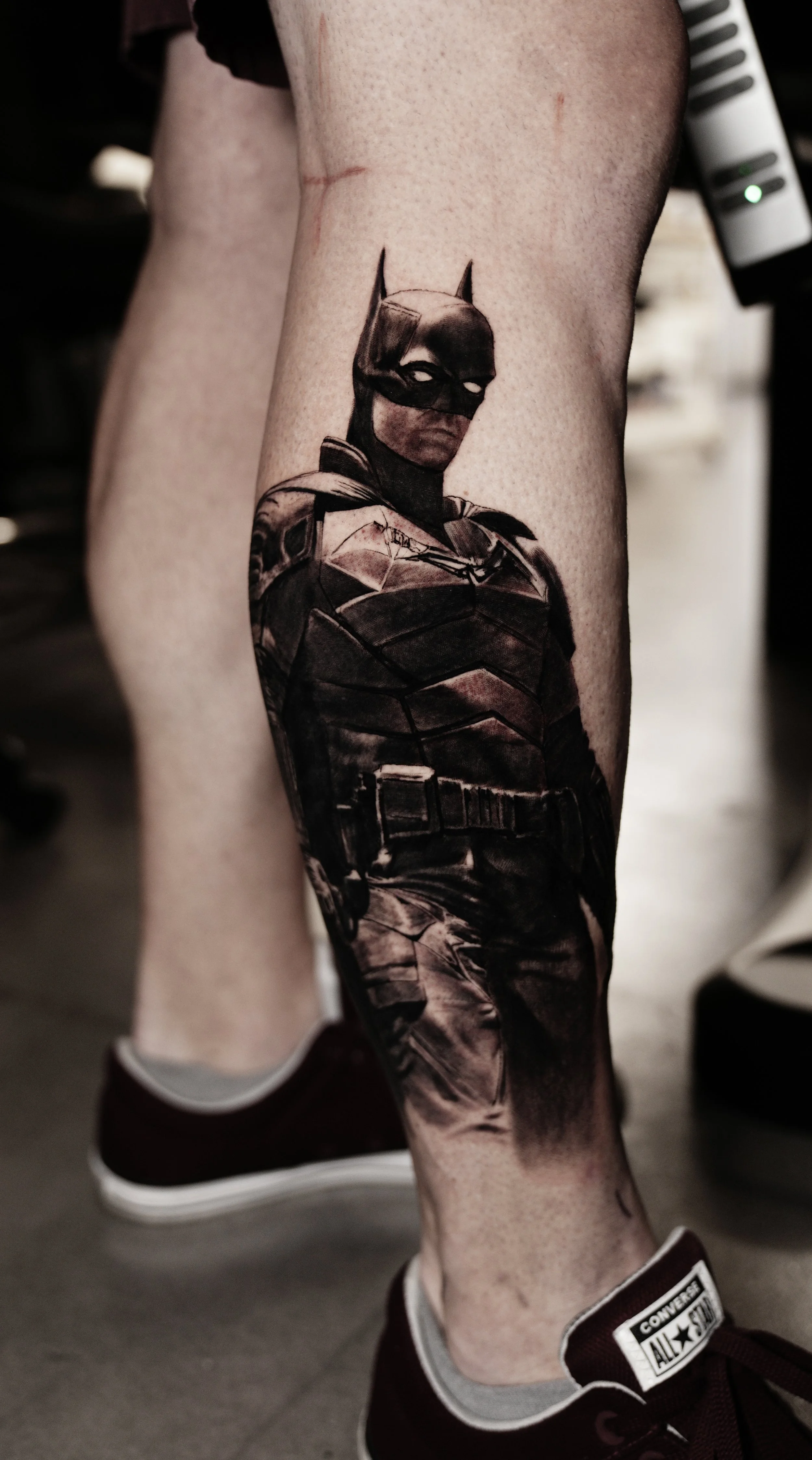 Tattoo of Batman on a person's calf, with a dark and shaded design highlighting Batman's face and upper body.