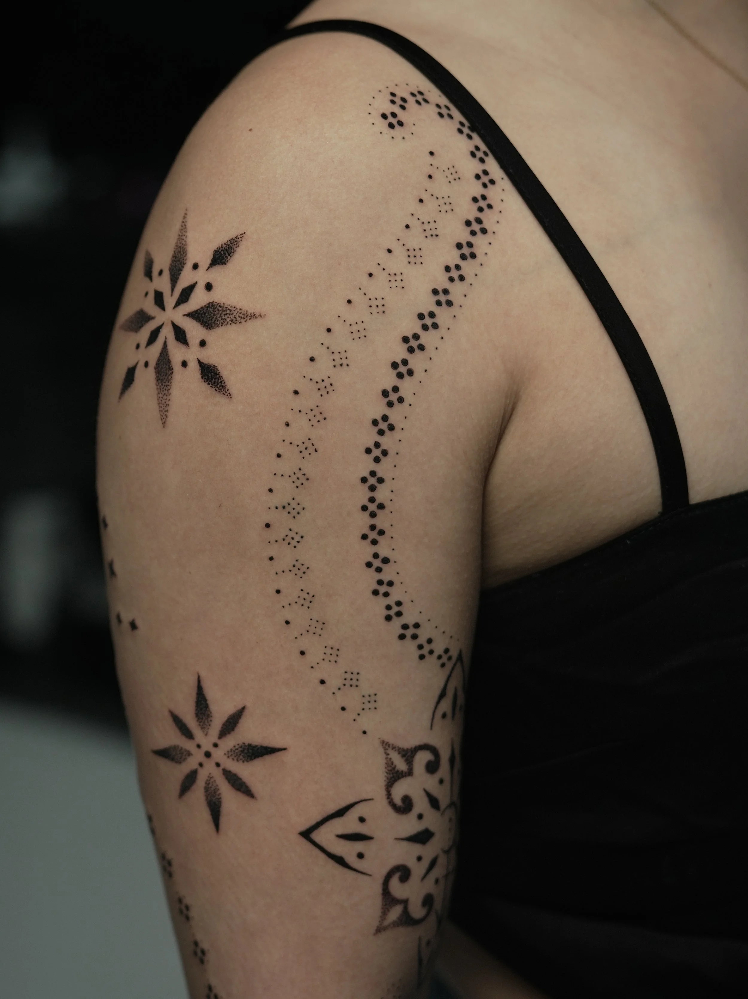 Tattooed upper arm with black ink designs including snowflake patterns, dotted lines, and abstract shapes.