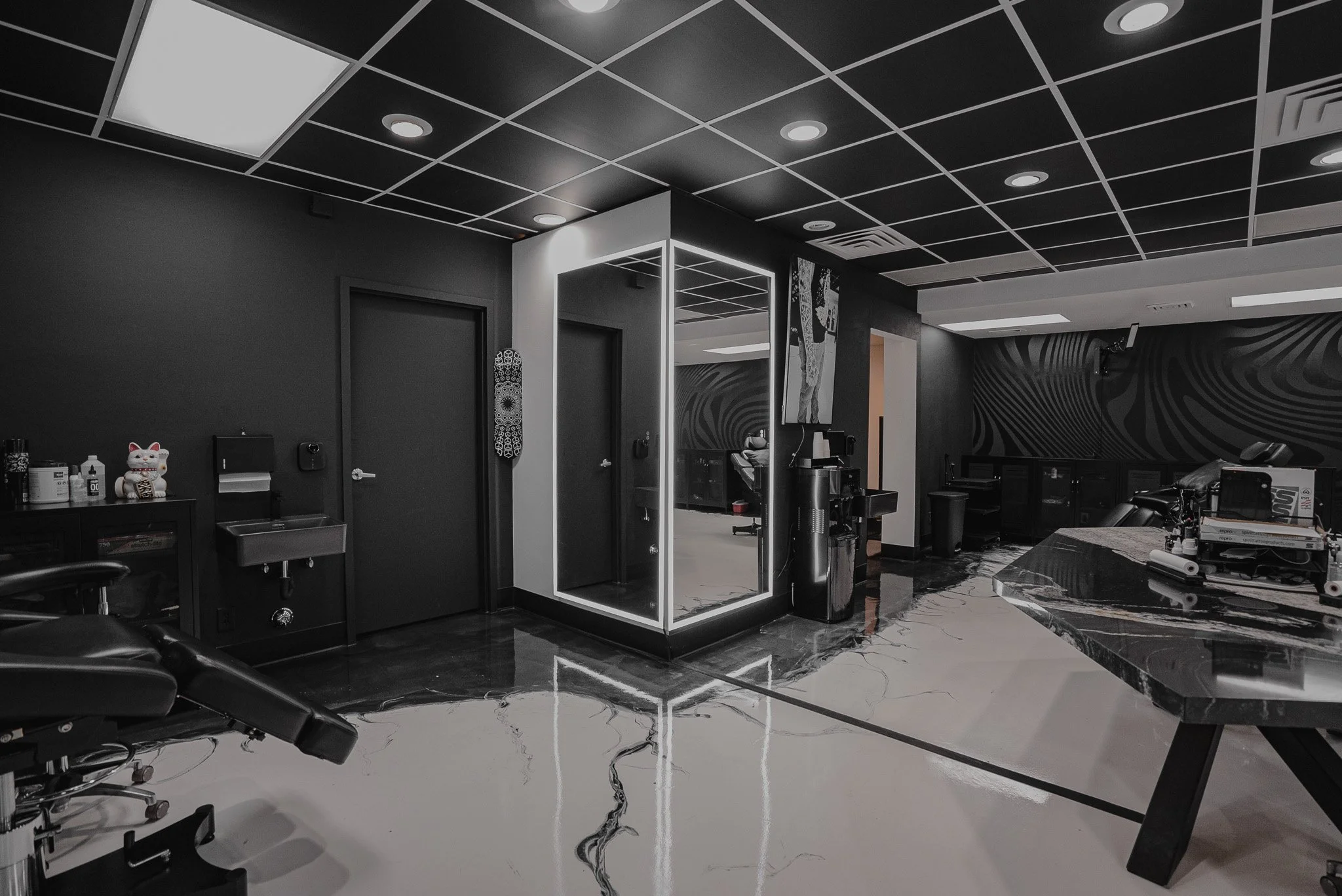 A modern salon with black and white decor. Contains a salon chair, sinks, a reception desk, and artistic wall designs.