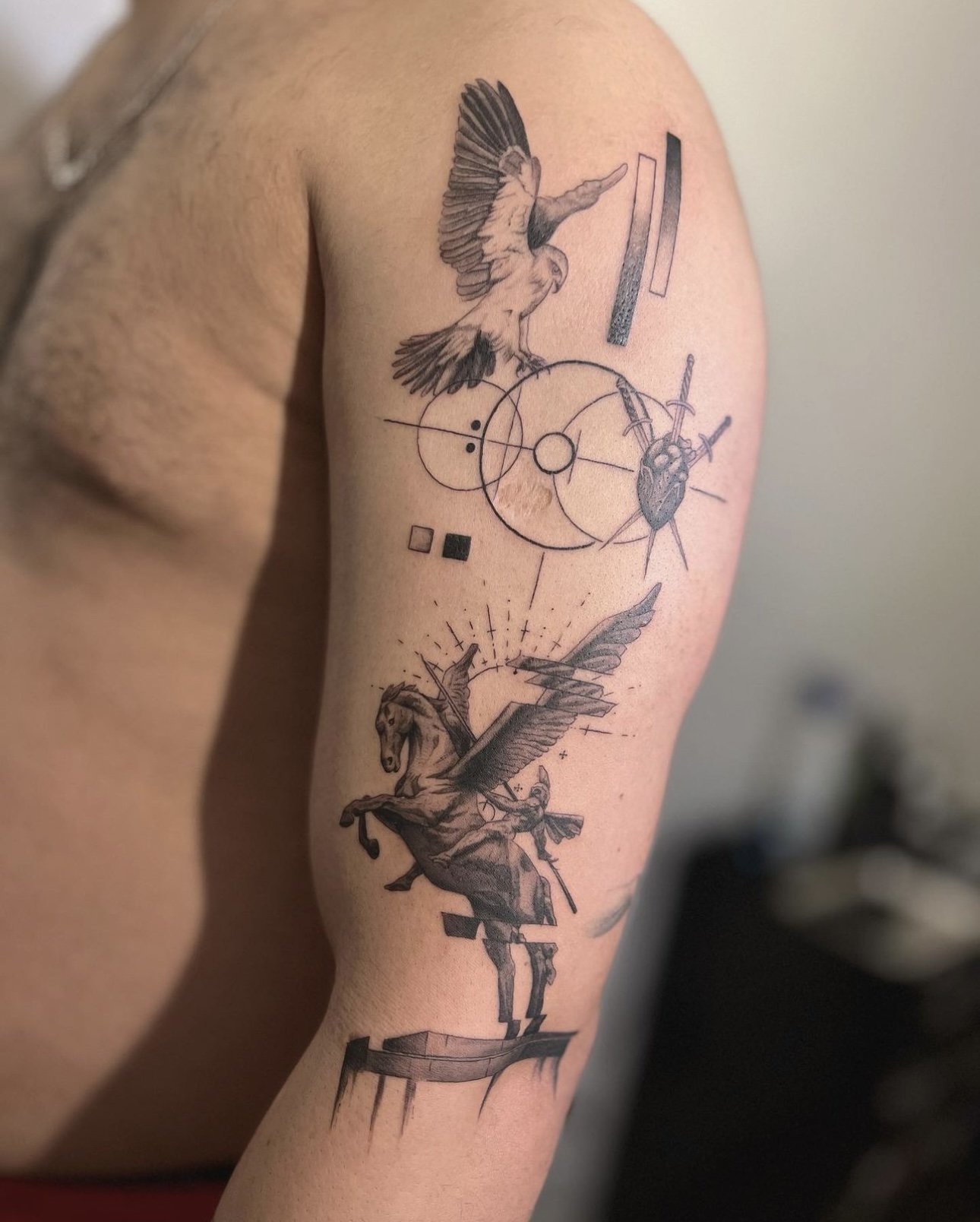 Tattoo featuring a bird, a winged horse, and geometric shapes on a person's upper arm.