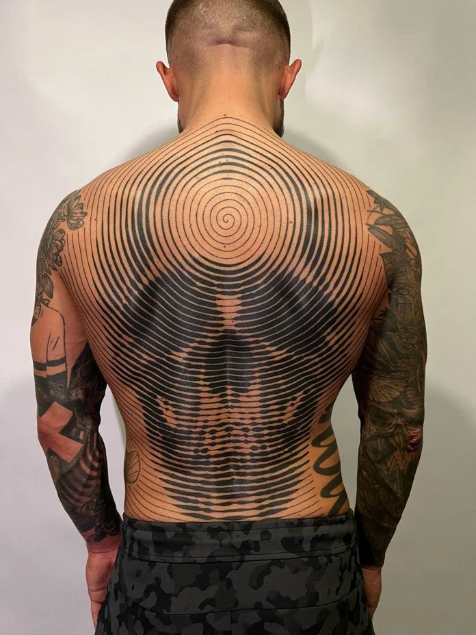Back view of a man with tattoos, showcasing a large black spiral tattoo covering most of his back.