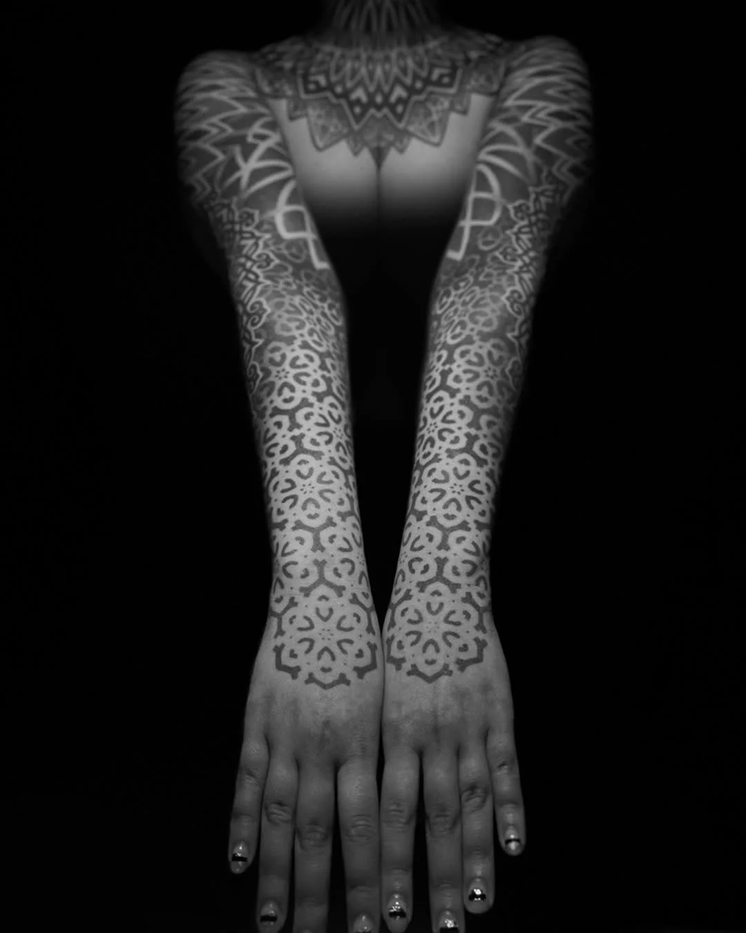 A person with tattoos on their arms and chest, lying face down on a black surface, with hands and fingers extended forward.