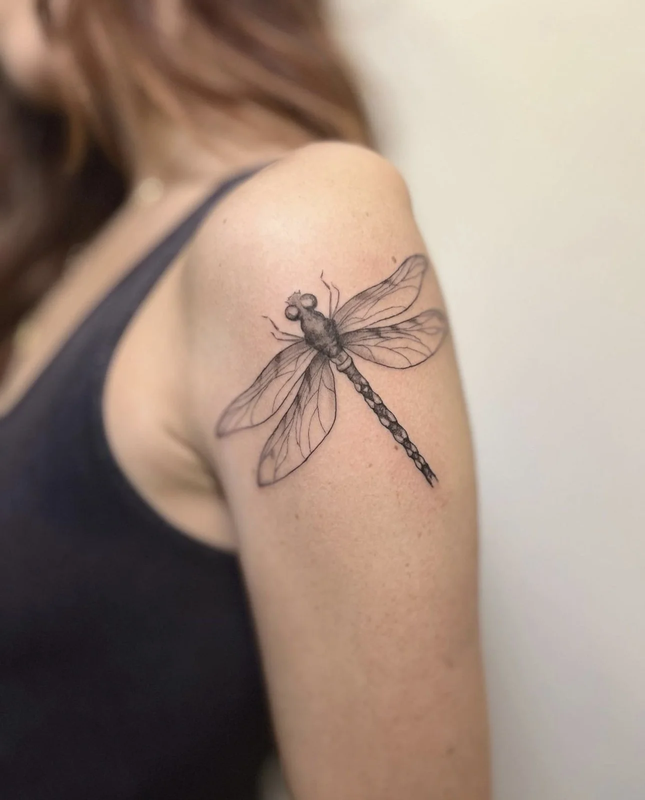 Black and gray tattoo of a dragonfly on a woman's upper arm