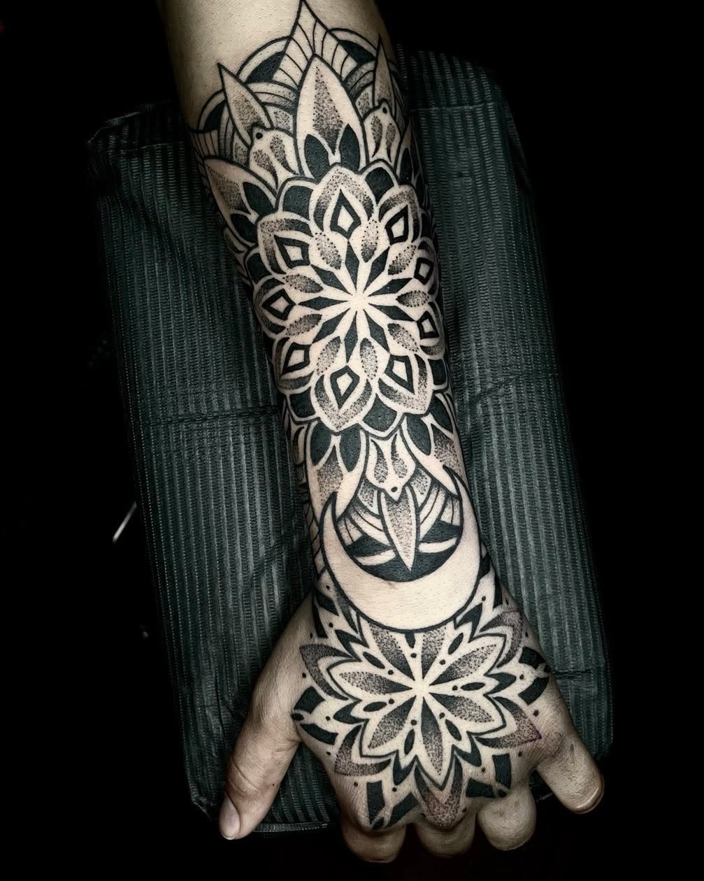 Black and gray intricate mandala tattoo on forearm and hand with floral and geometric designs