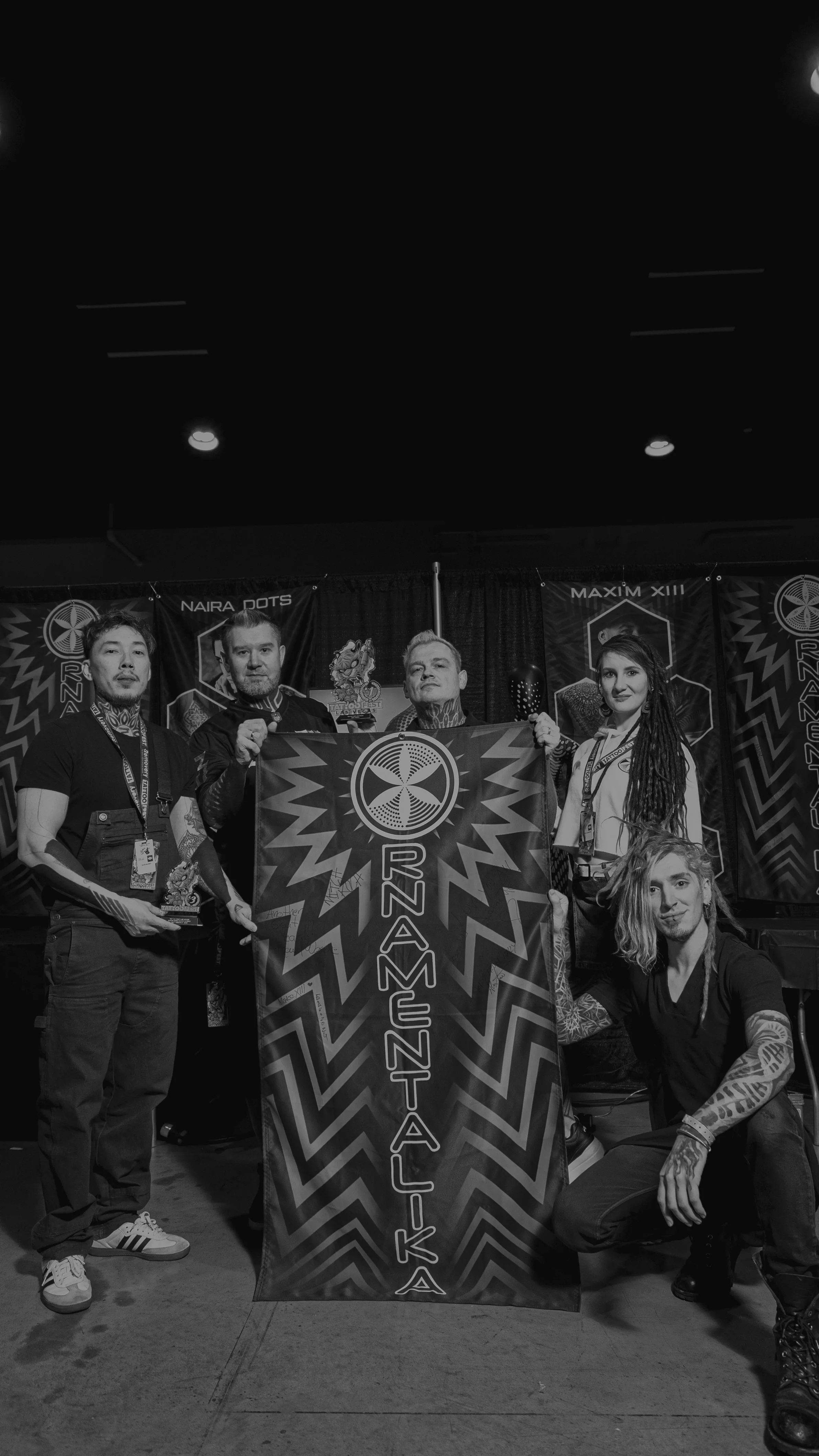 Group of five people holding a flag with the text "RNZRSTA" and logo at an event, with banners in the background reading "NAIRA DOTS" and "MAXIM XIII."