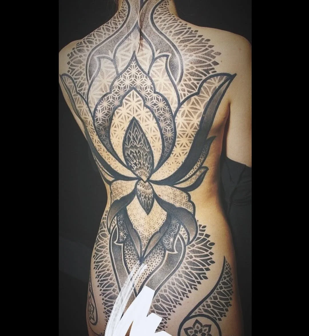 A large black and white geometric tattoo of a lotus flower covers the person's chest, stomach, and part of their right arm.