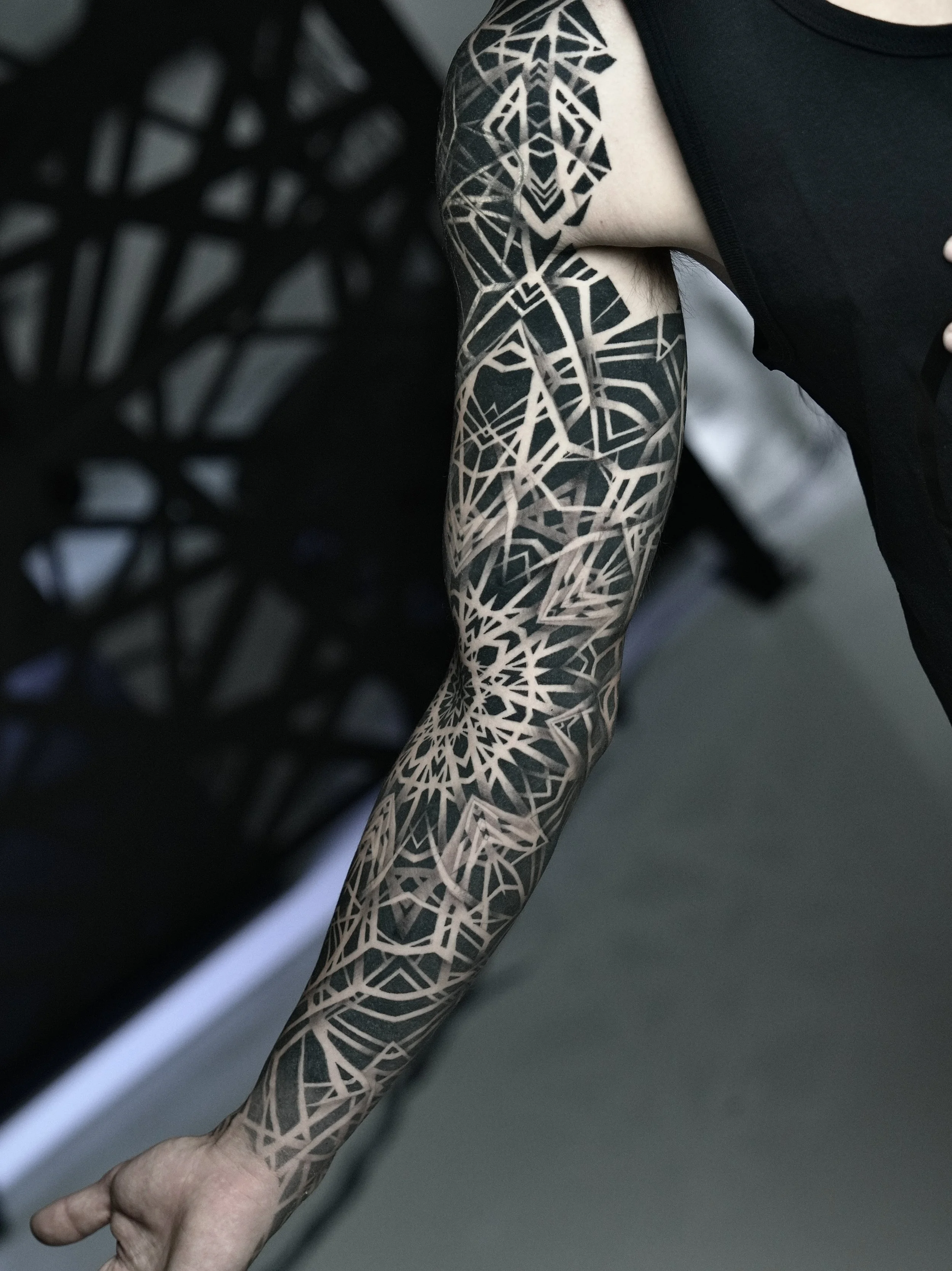 Close-up of a person's arm with a large black and grey geometric tattoo extending from shoulder to wrist.