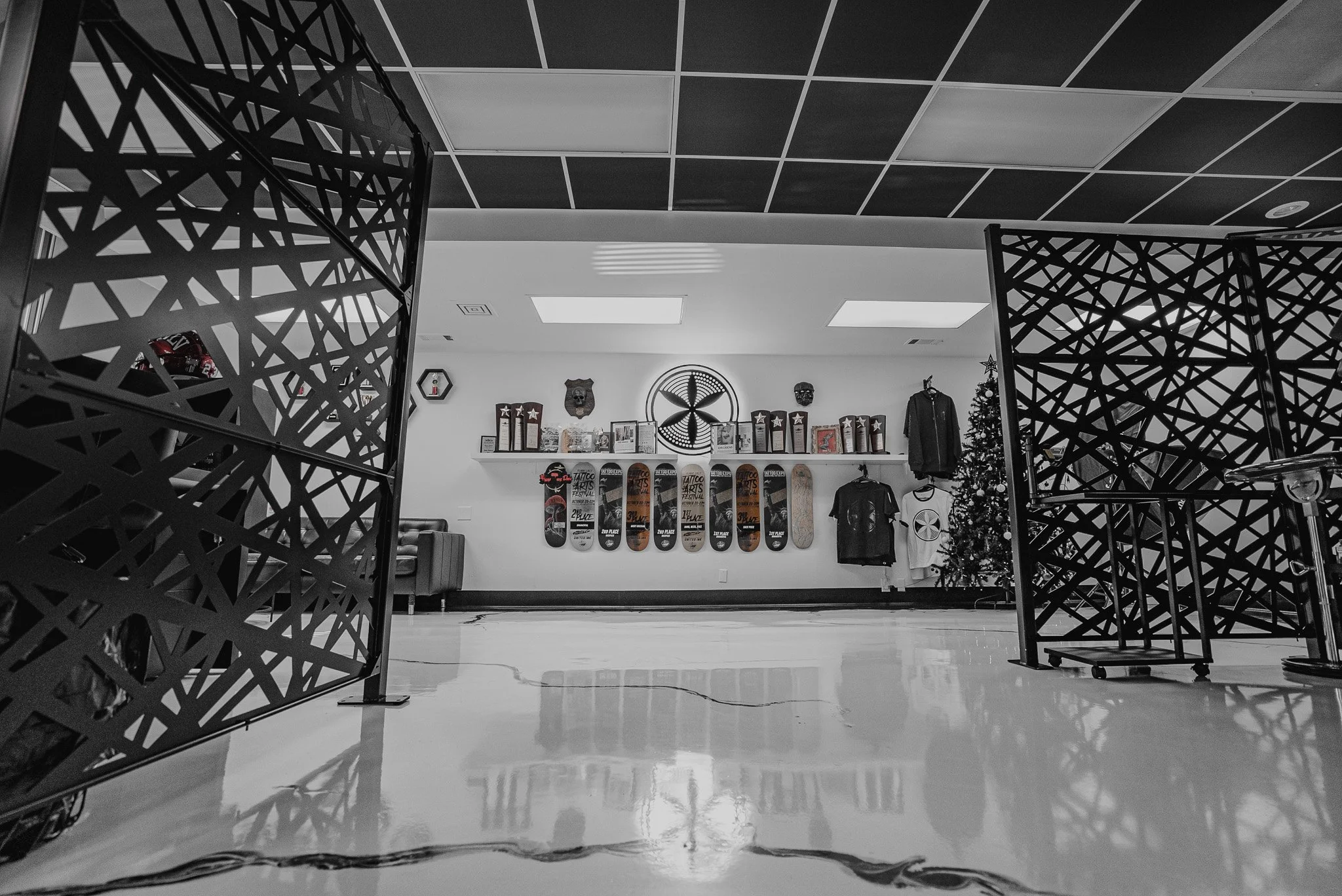 Indoor skate shop display with skateboards mounted on the white wall, clothing items, trophies, and decorative masks, view from a low angle.