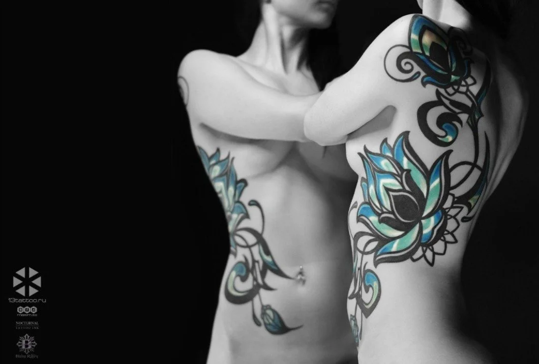 Two tattooed women with floral tattoos on their bodies pose against a black background, with one woman partially concealed and both facing away from the camera.