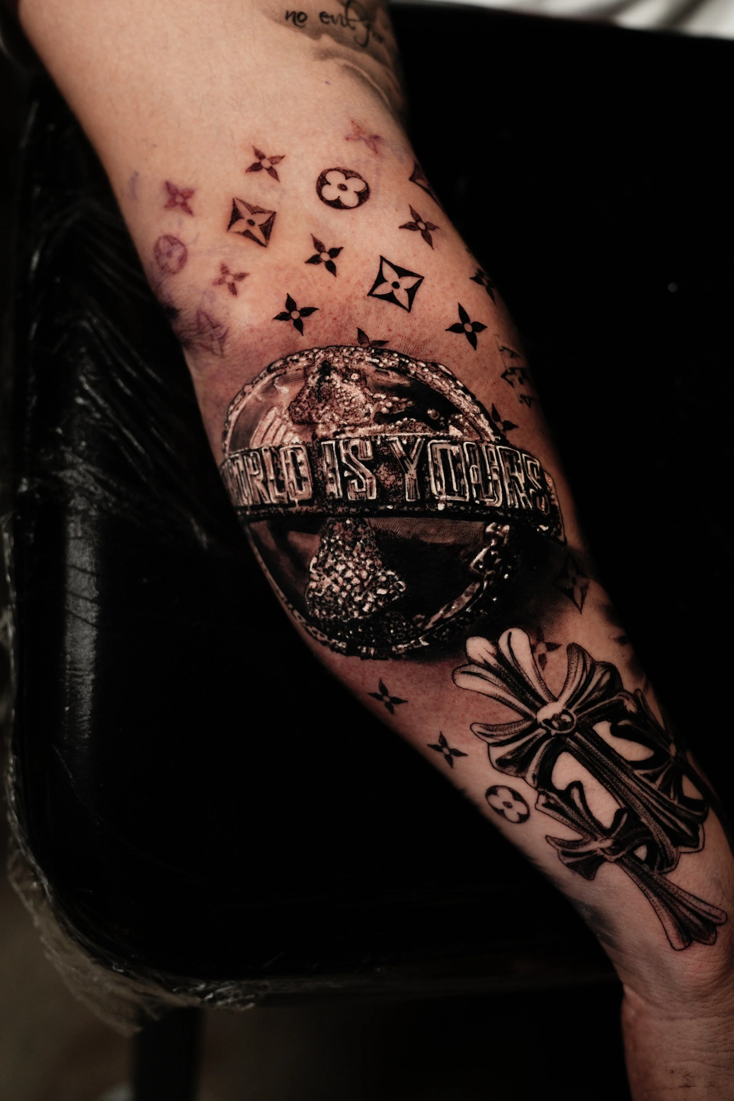 Tattooed arm with symbols including a peace sign, floral designs, and a circular logo with the words "WORLD AS YOU".