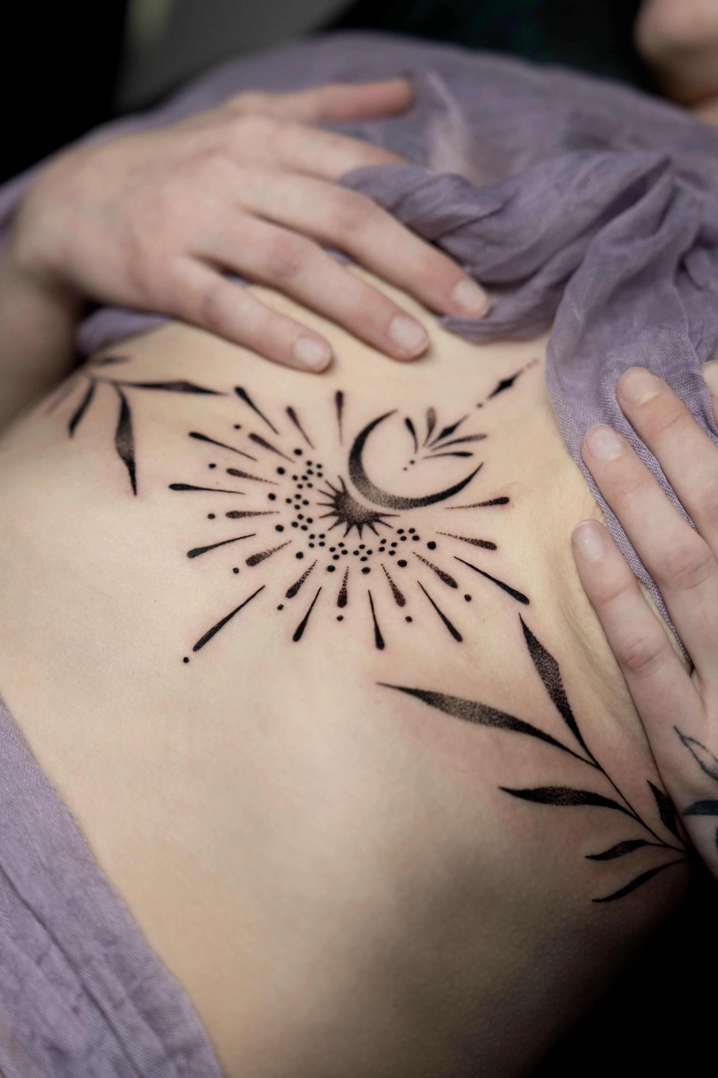 Tattoo of a crescent moon and star with sunrise or rays around it on person's side torso.