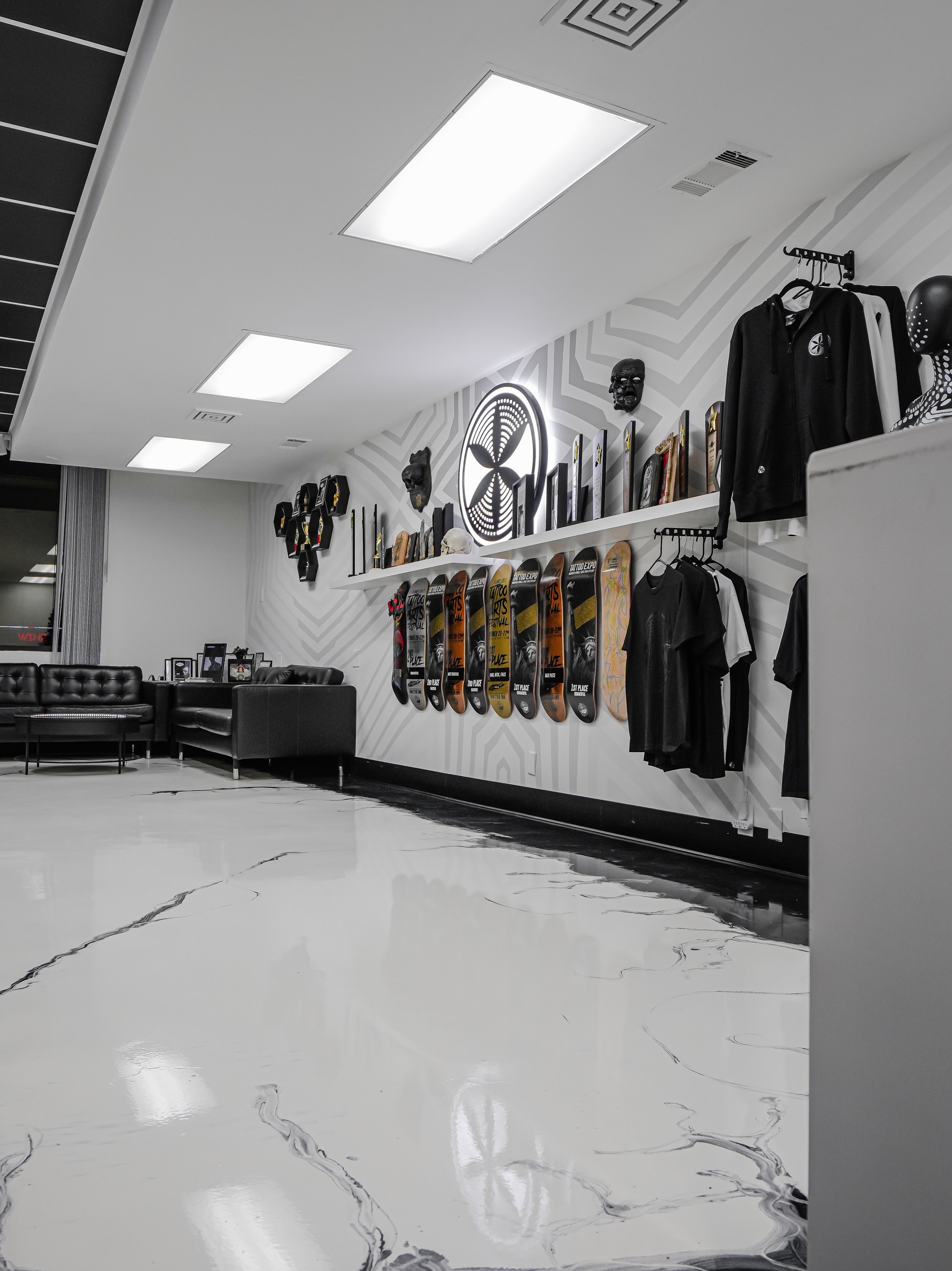 Skateboard shop with skateboards displayed on a wall, black mannequins, and clothing for sale, illuminated by ceiling lights.