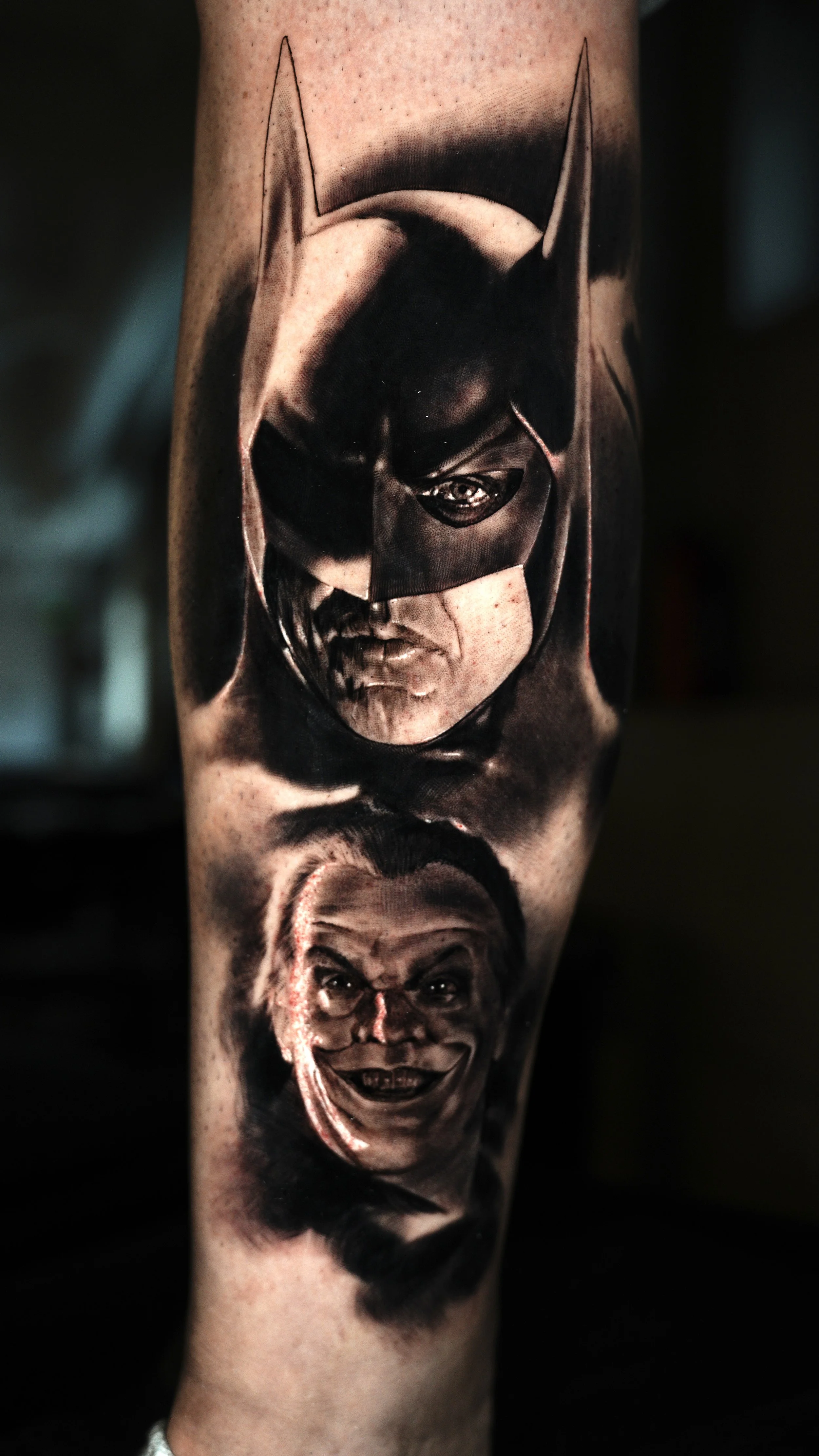 Tattoo of two faces, one Batman and one Joker, on a person's arm.