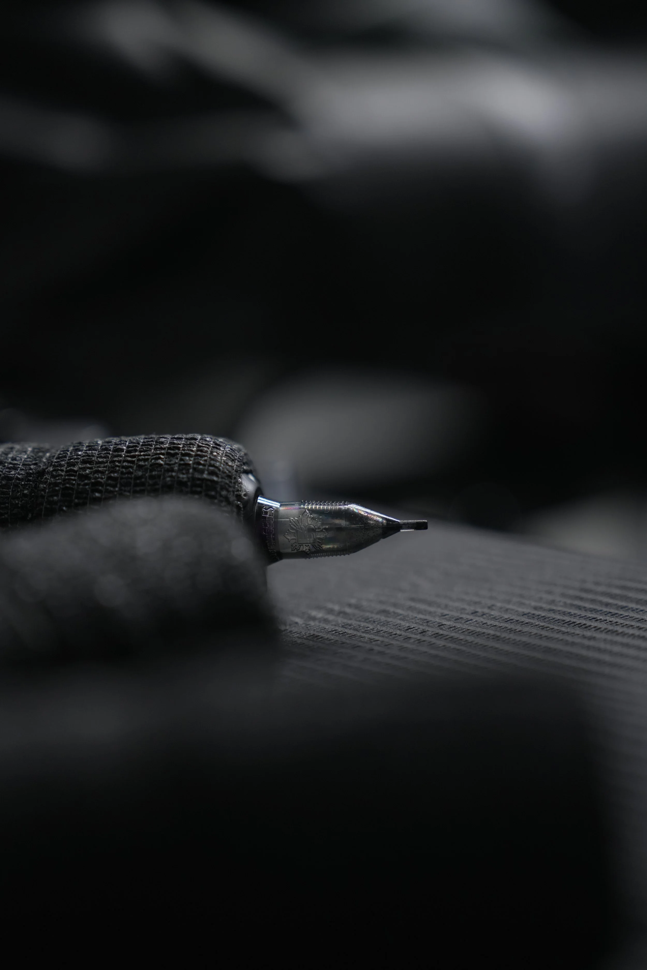 Close-up of a tattoo machine needle on dark textured surface with a gloved hand in the background.