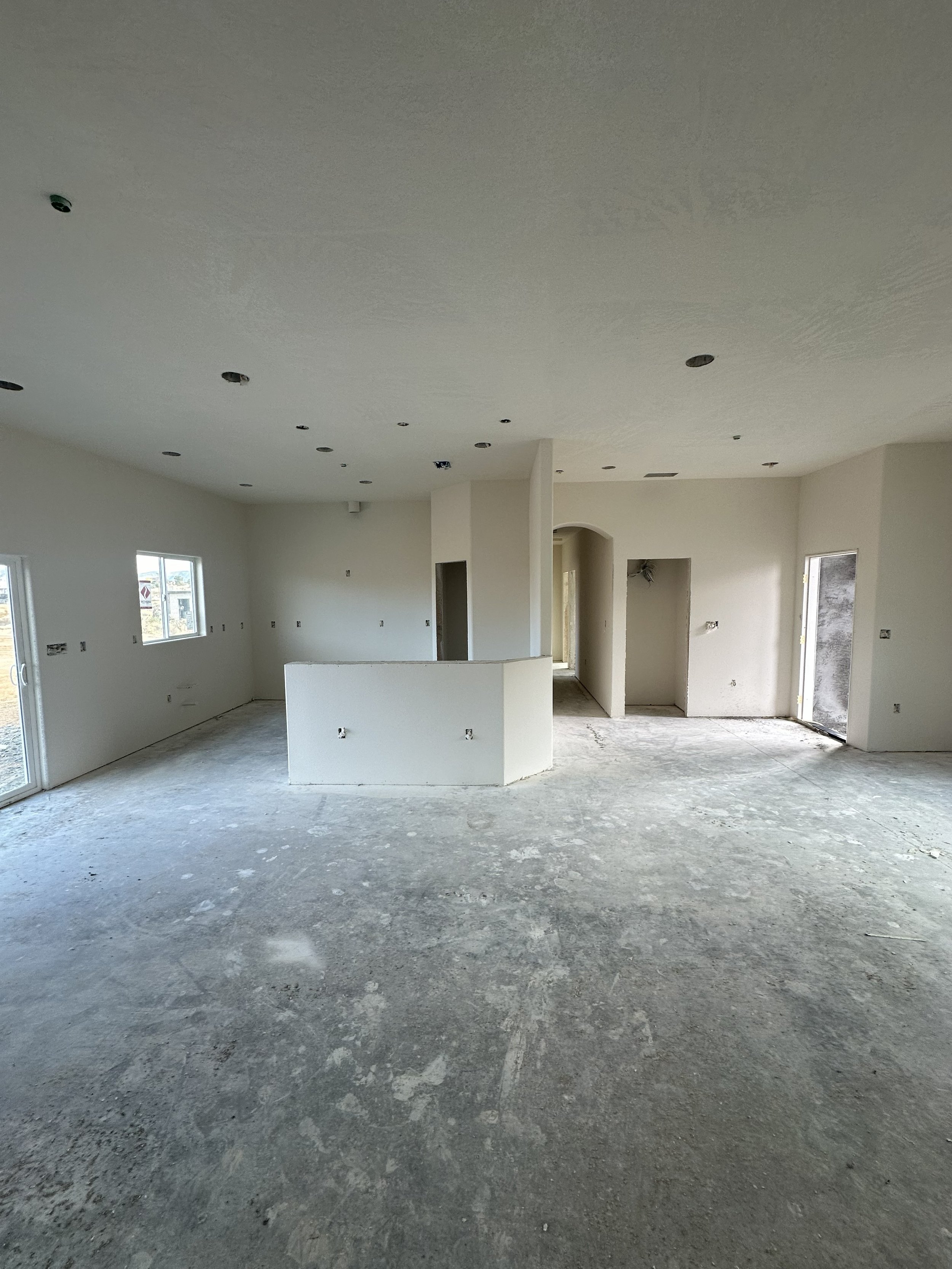 Interior of an unfinished house with white walls, exposed concrete floor, and missing fixtures.