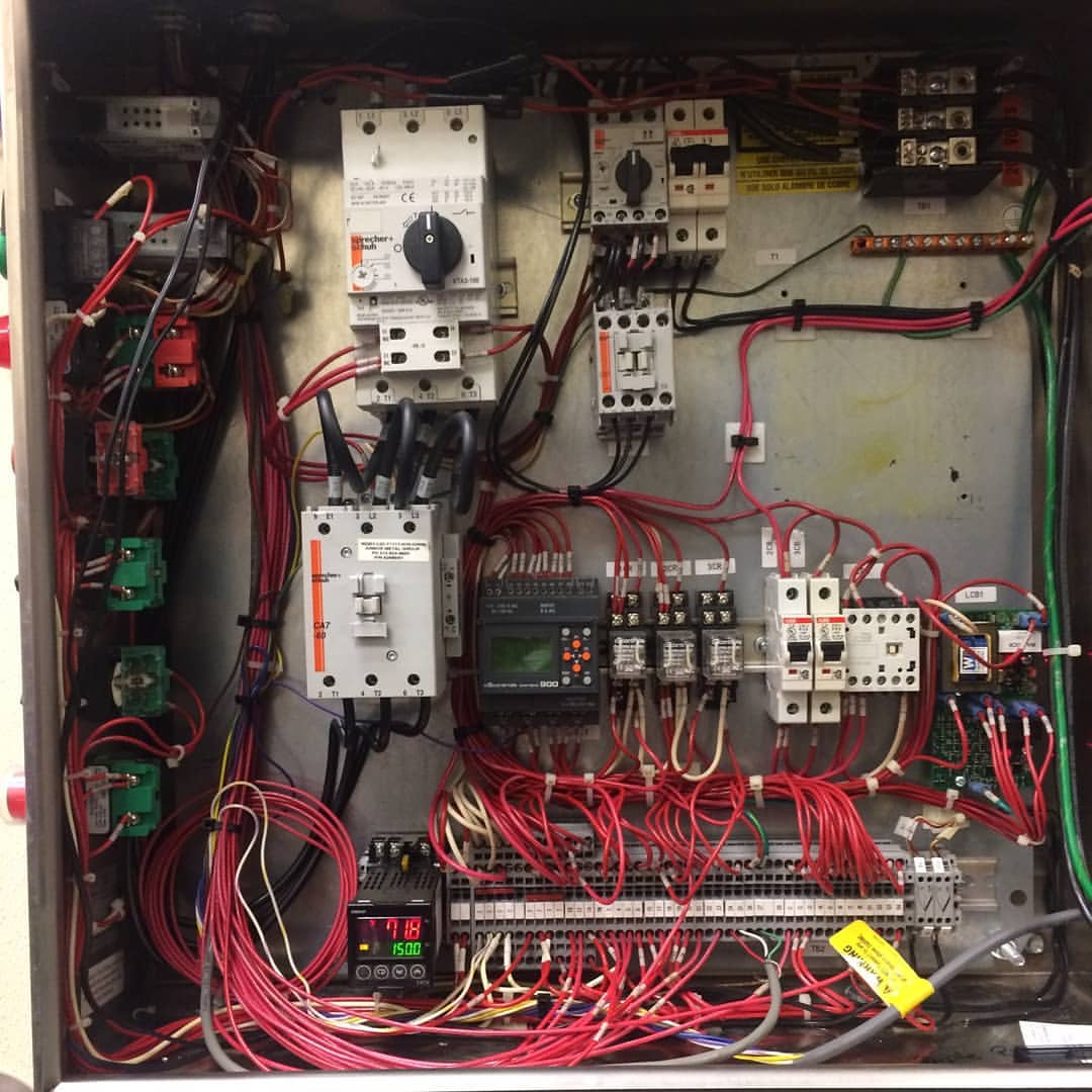 Electrical control panel with various wires, switches, and circuit components inside a metal box.