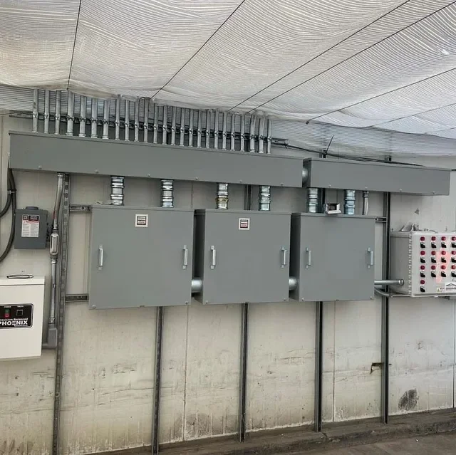 Electrical panels and conduit boxes mounted on a concrete wall in an industrial setting.