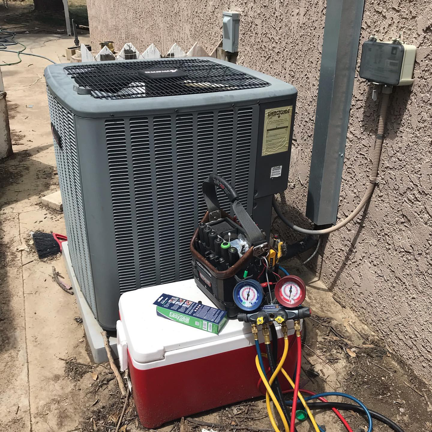 Air conditioning unit outside a building with repair tools, gauges, and a cooler nearby.
