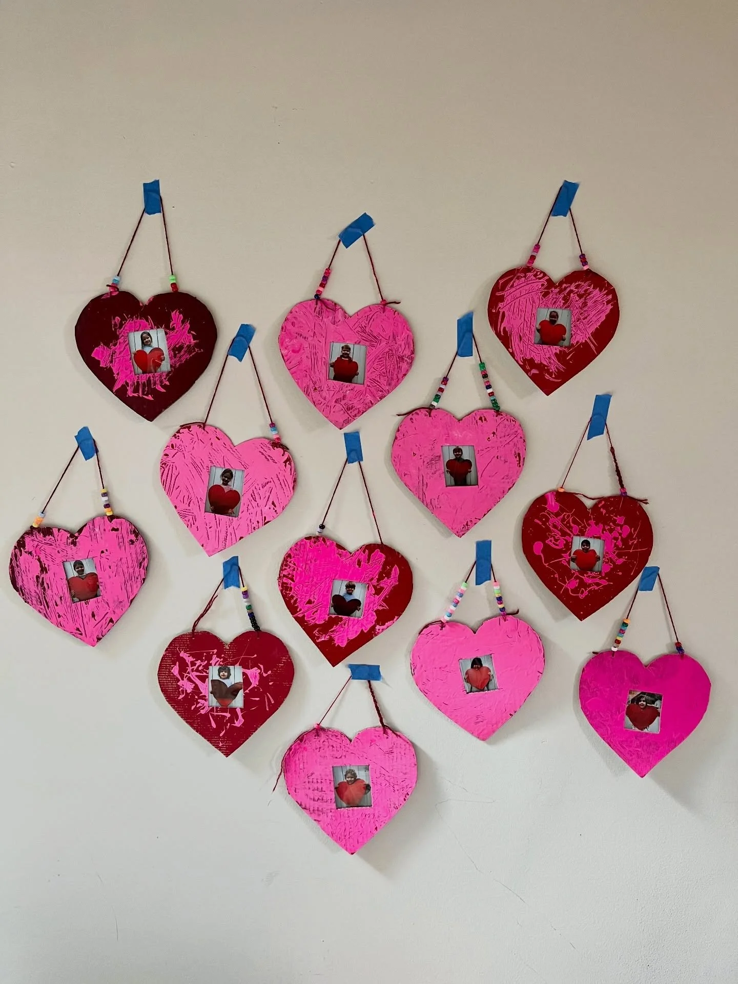 Valentine presents for preschool families. Cardboard heart, tempera paint splattered and spread with a plastic knife, yarn, pony beads and Polaroids.
