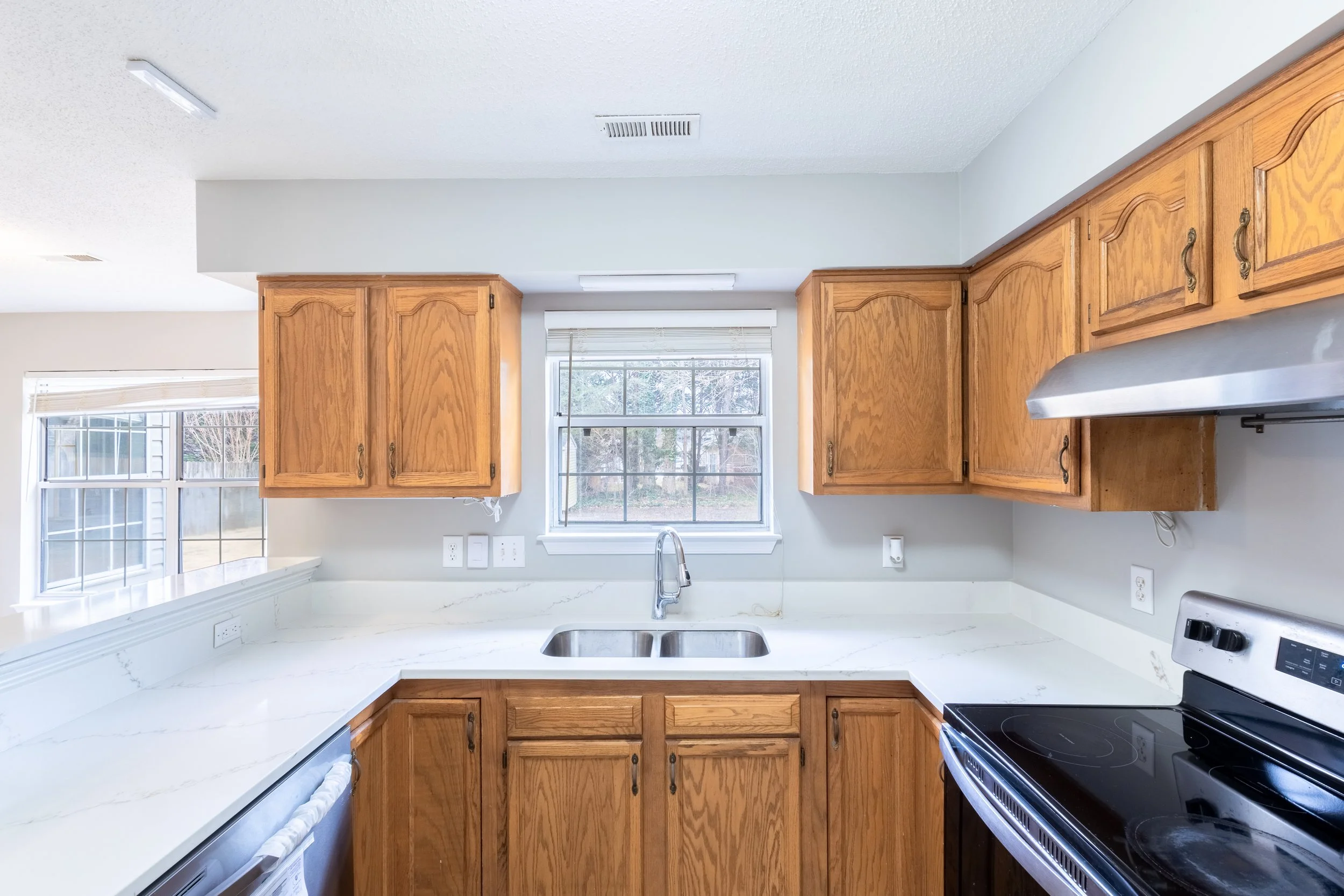 Kitchen with wooden cabinets, white marble countertops, a window above the sink, a stainless steel range hood, and an electric stove.