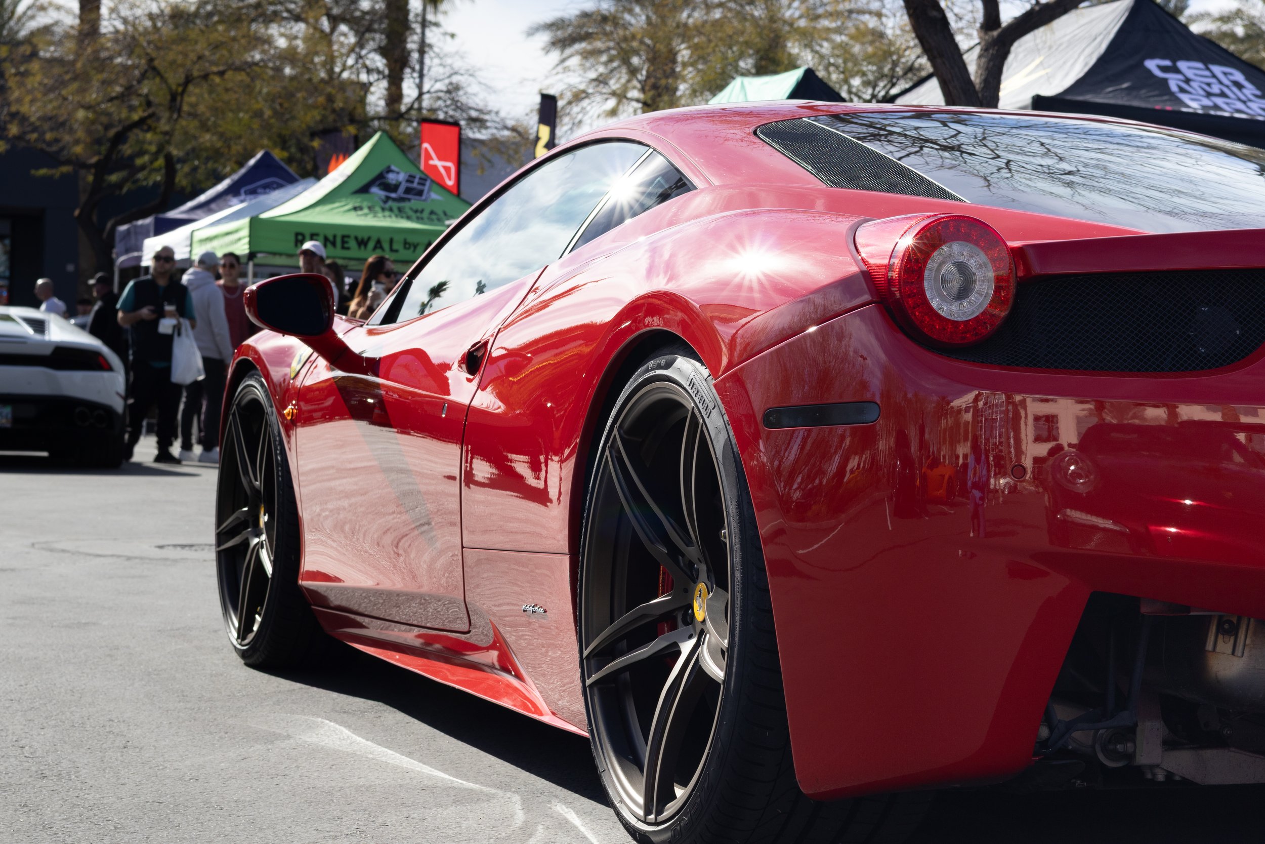 Close-up of a red sports car at an outdoor car event, with people and tents in the background. Car meet. Cars and coffee. Rollers. Stills. Detail shots. Brand awareness. Ferrari 458