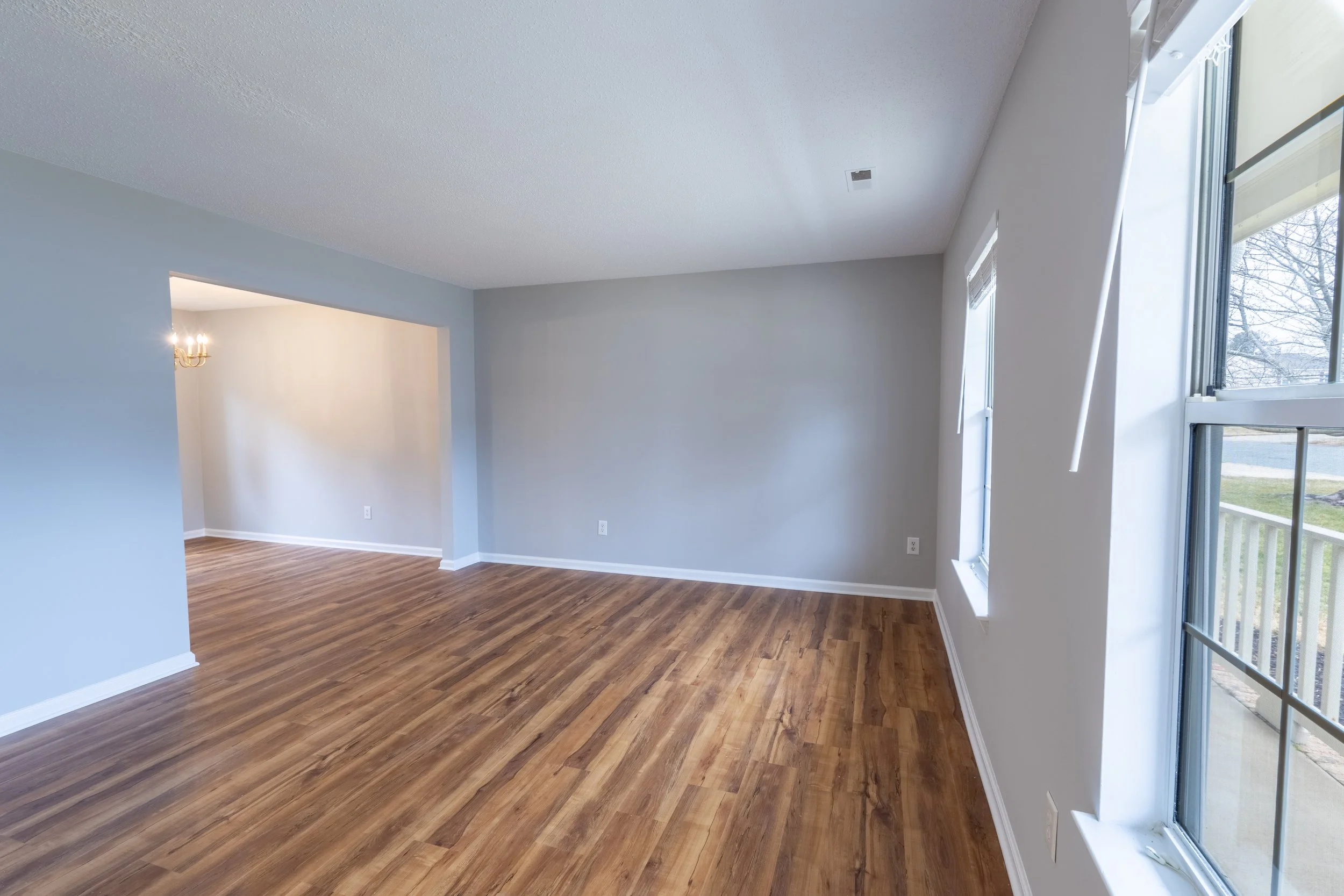 Empty living room with hardwood floors, light blue and white walls, and large windows.