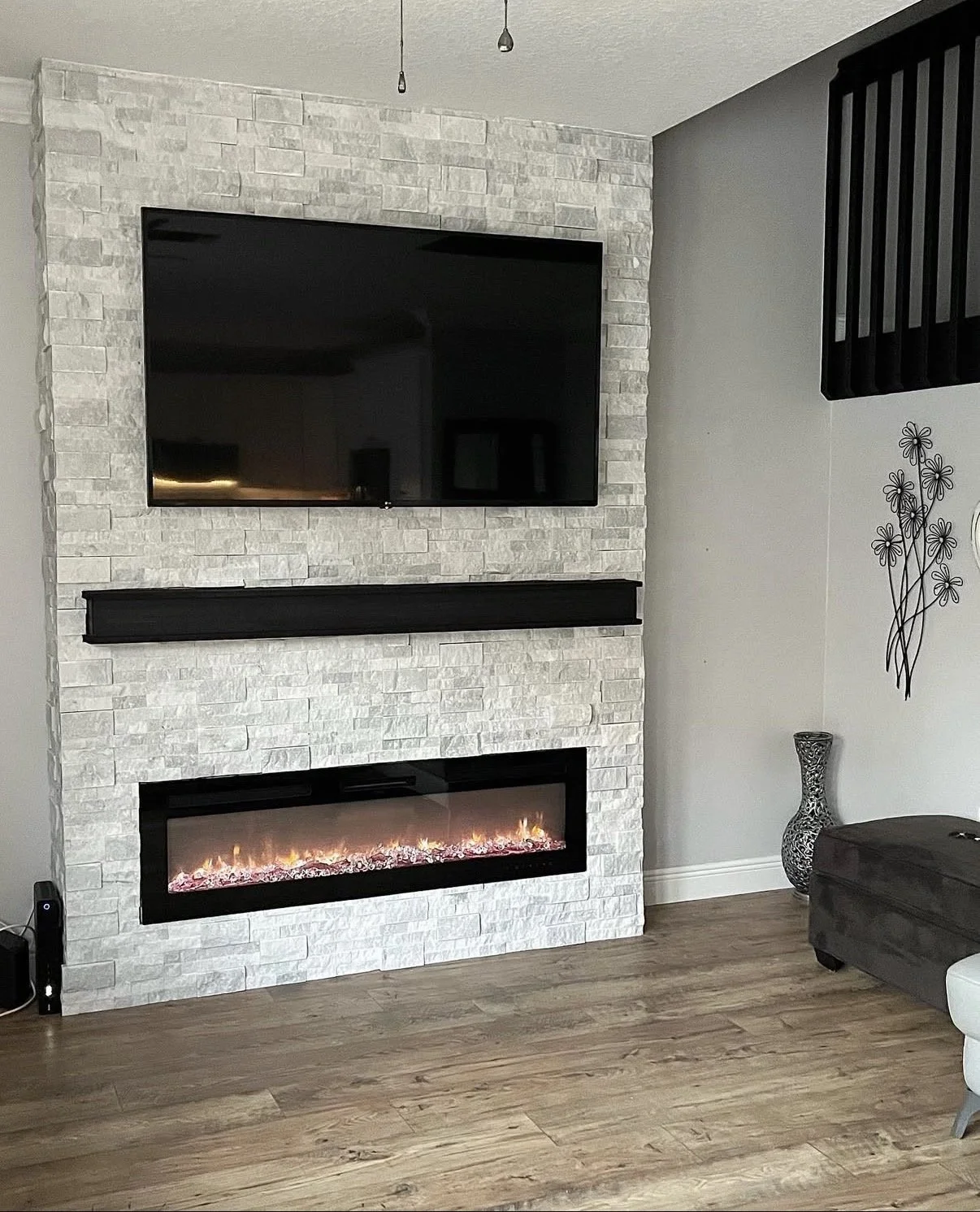 Living room with modern fireplace, mounted TV on a white stone wall, decorative vase, and wall art of flowers.