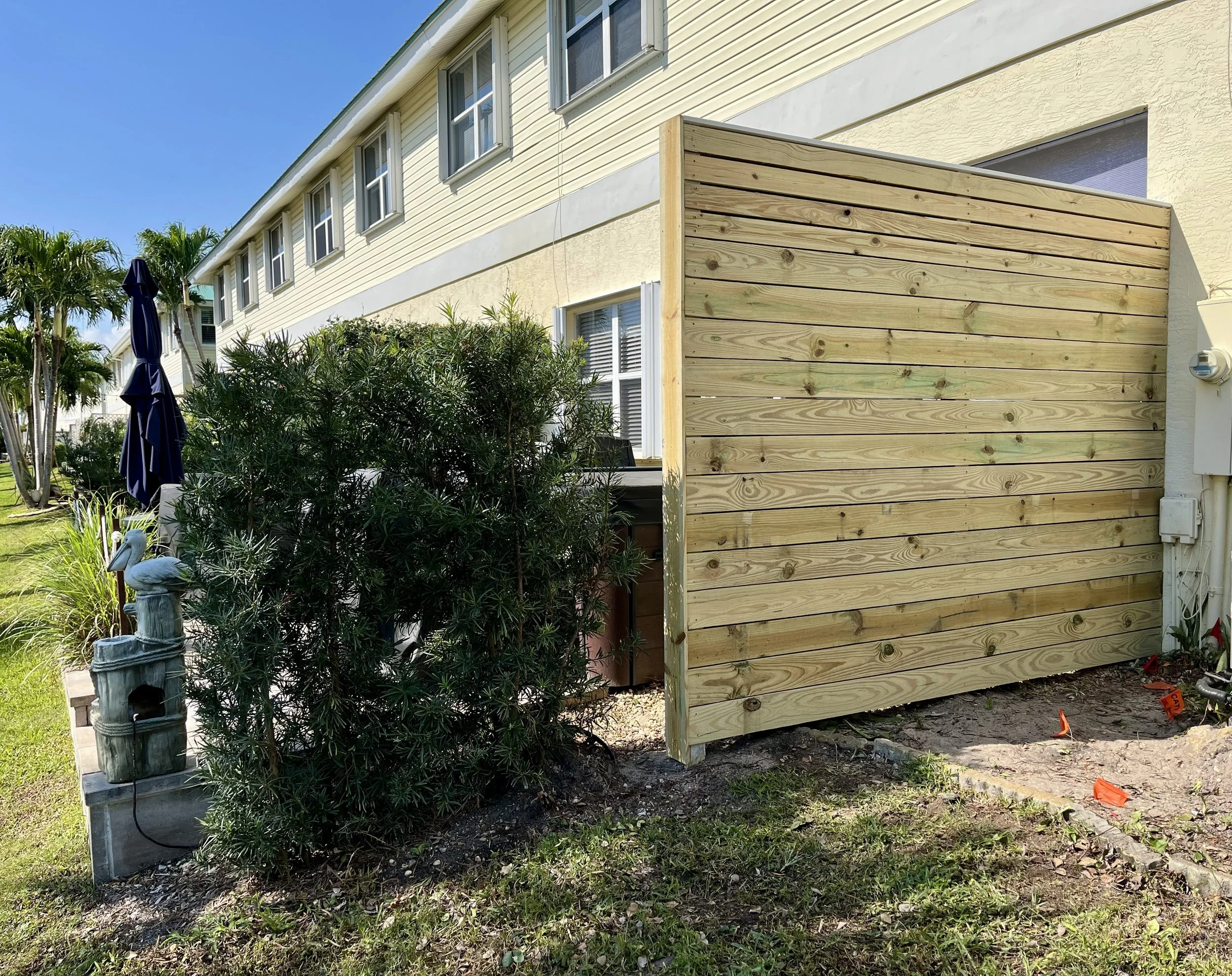 Image of a wooden privacy screen or fence outside a yellow house, next to potted plants on a patio.