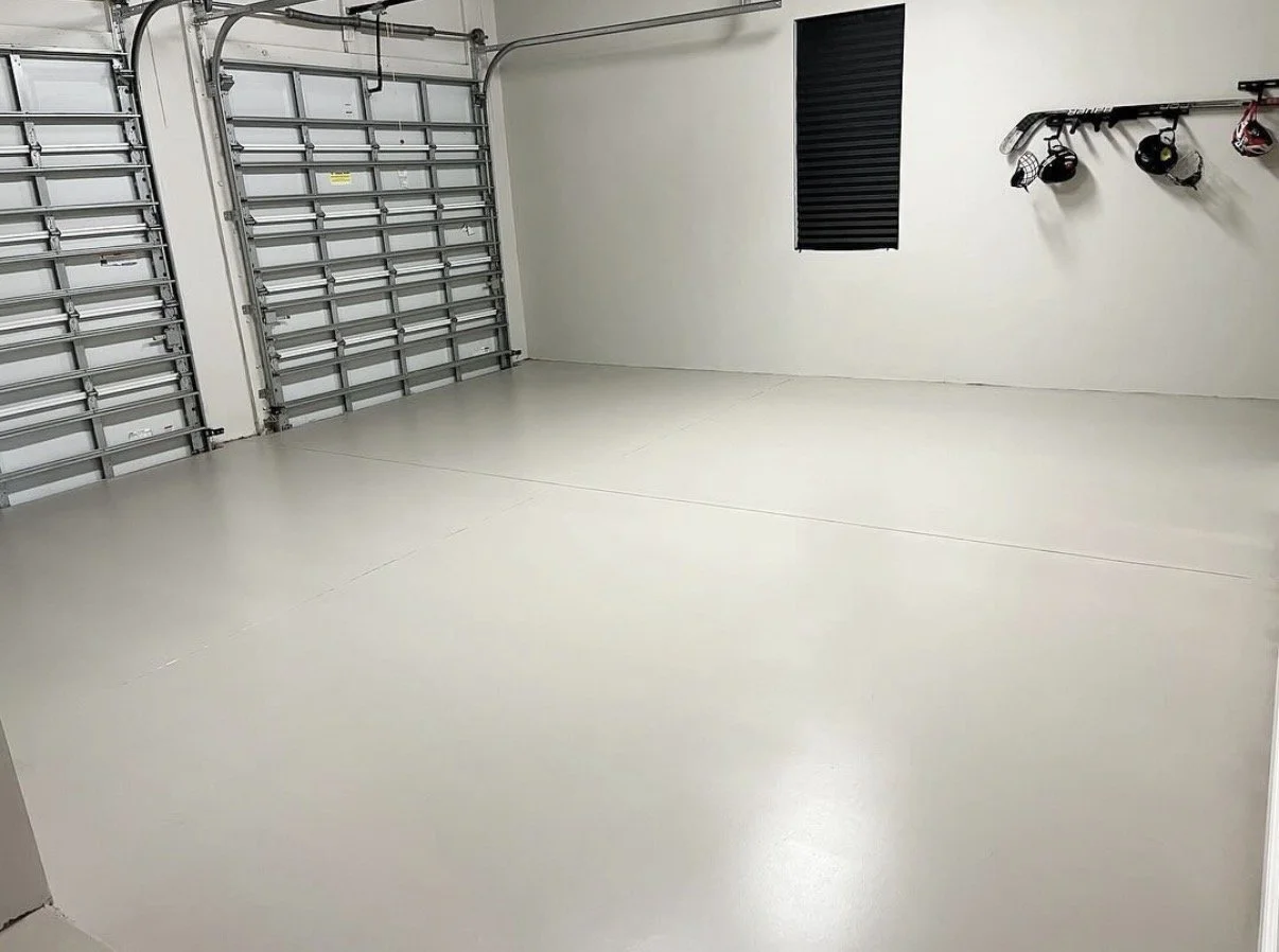 Empty garage with two closed metal garage doors, a small window with black blinds, and wall-mounted hooks with helmets and workout equipment.