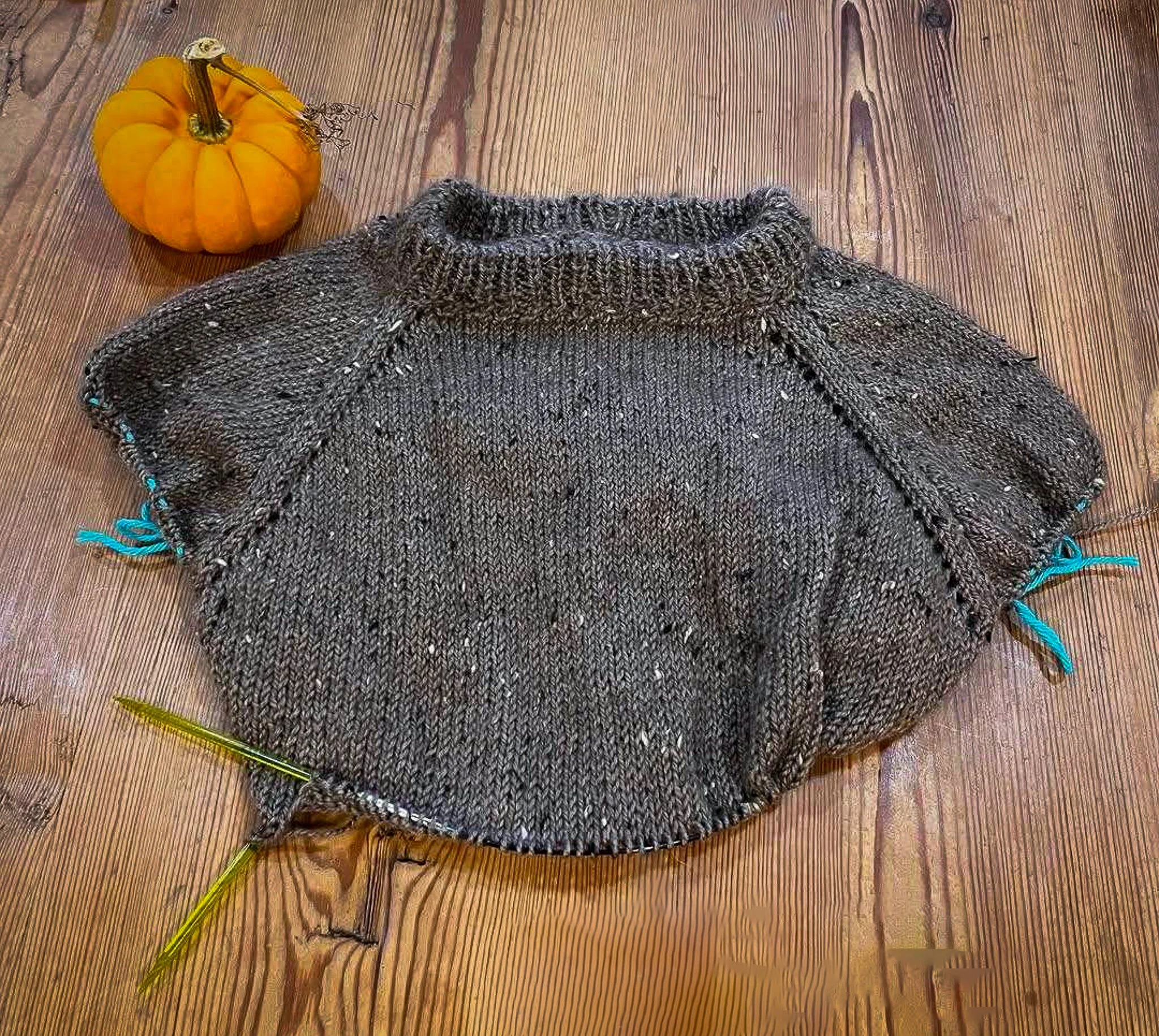 An in-progress dark grey knitted sweater with brassy colored knitting needles
