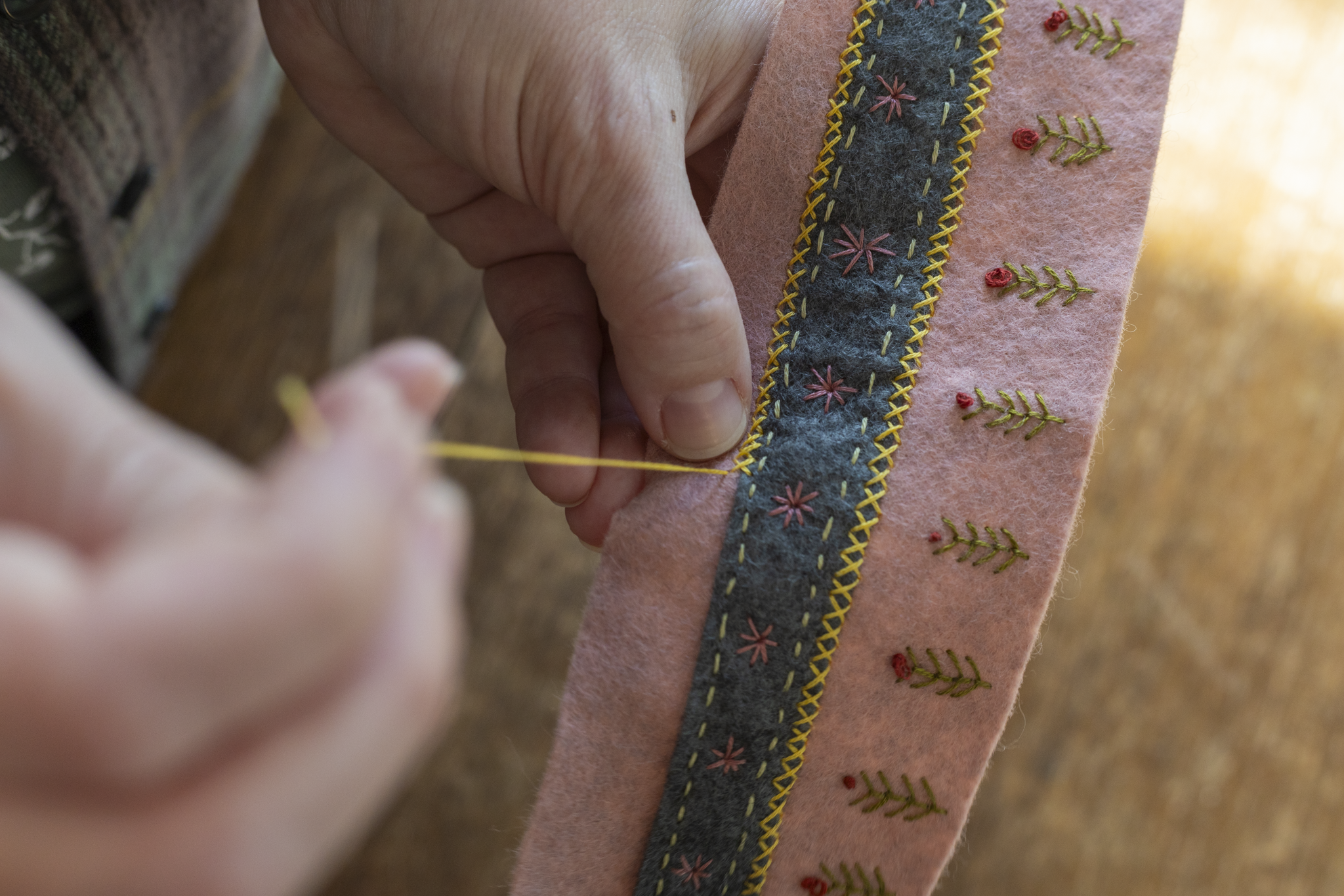 A person using yellow thread to stitch a felt craft project