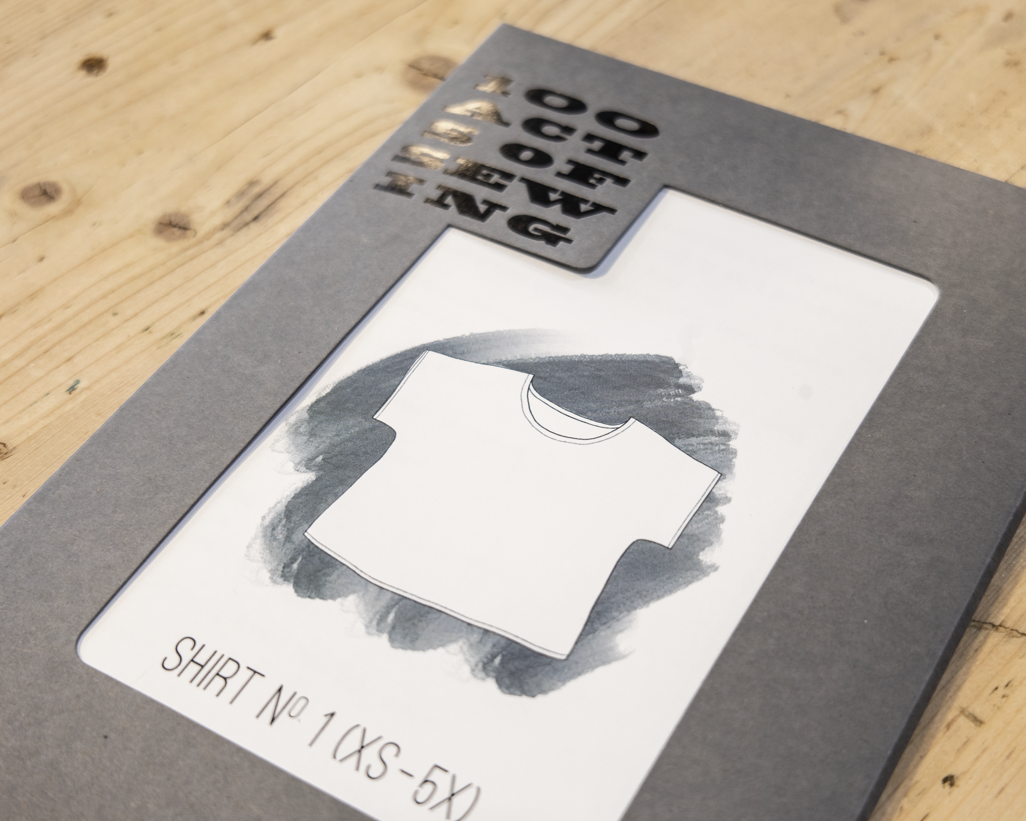 Grey packaging that holds a simple, classic pattern for a shortsleeved "Shirt Number One" from patternmaker brand 100 Acts of Sewing