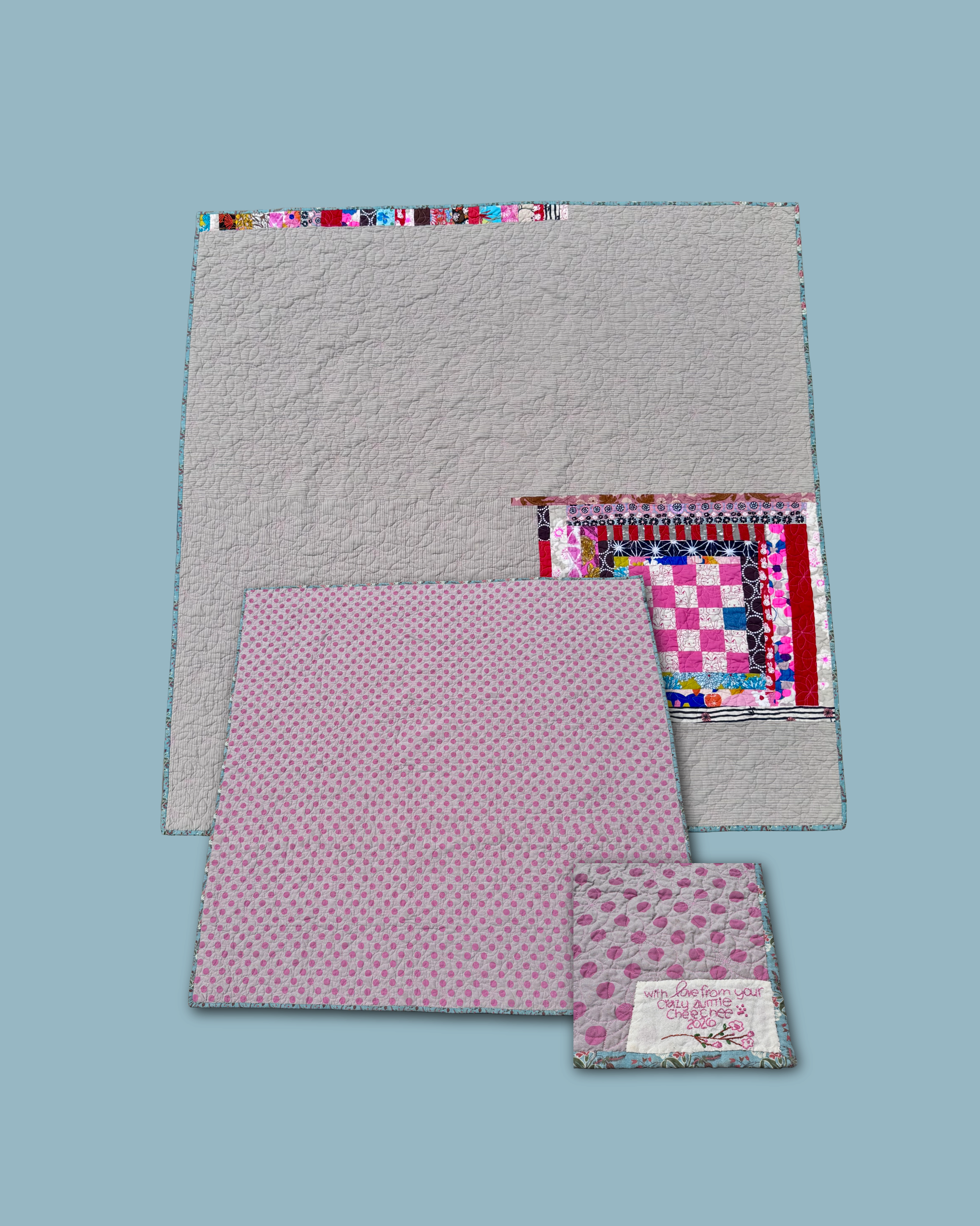 Front and back views of a baby quilt made with striped fabric on the front and pink polka dotted chambray fabric on the back. Bound with material featuring a floral pattern against a blue background.