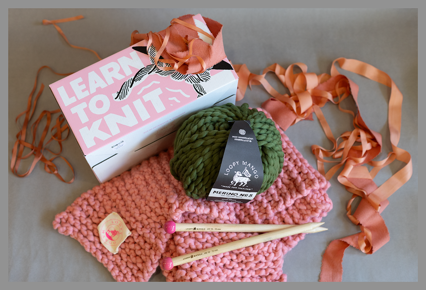 Learn to Knit kit with wool yarn in pink and green with knitting needles.