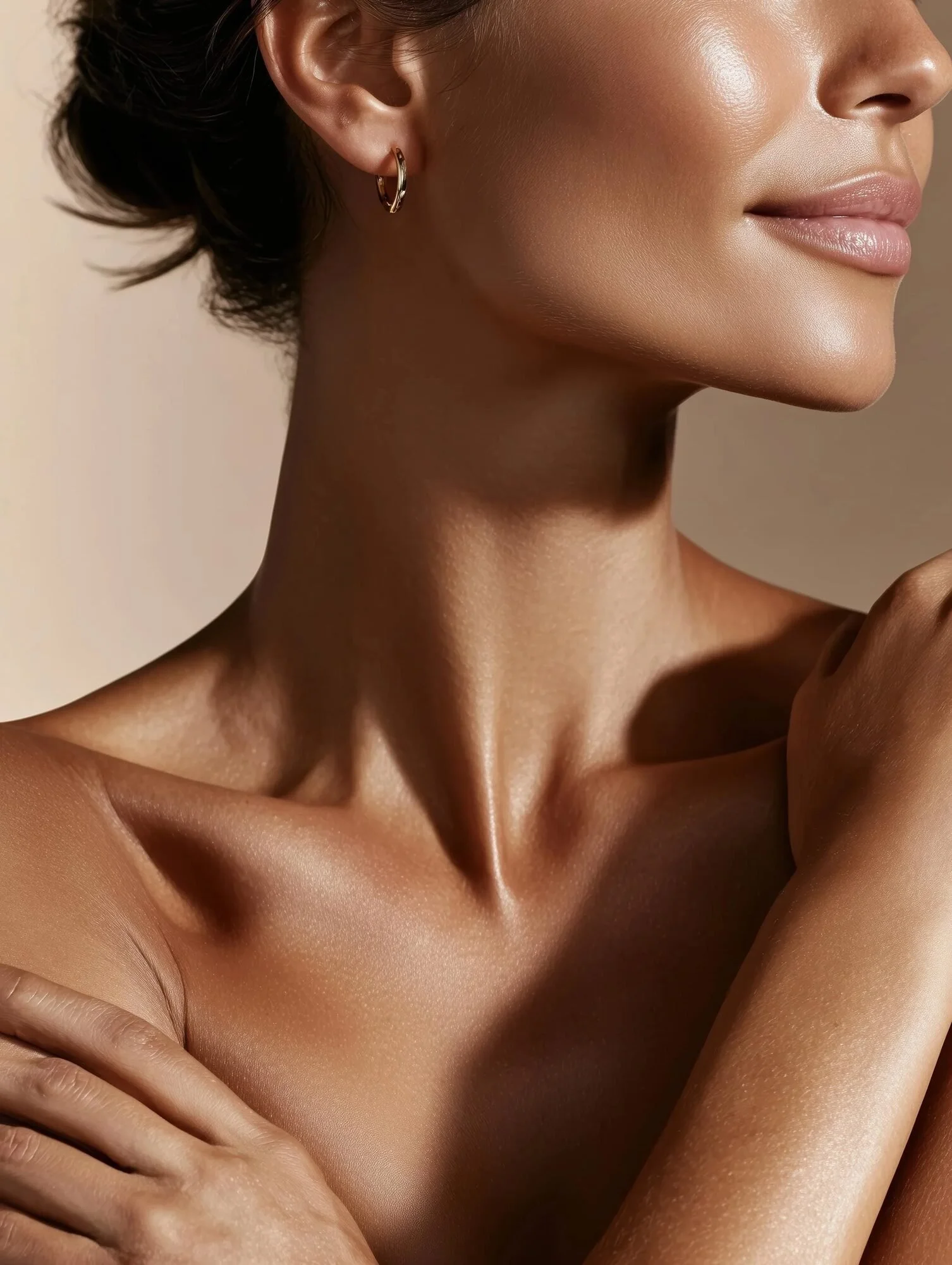 Close-up beauty portrait of a woman in warm, golden light, highlighting glowing skin, elegant facial contours, her neck and shoulders, and a delicate gold hoop earring.