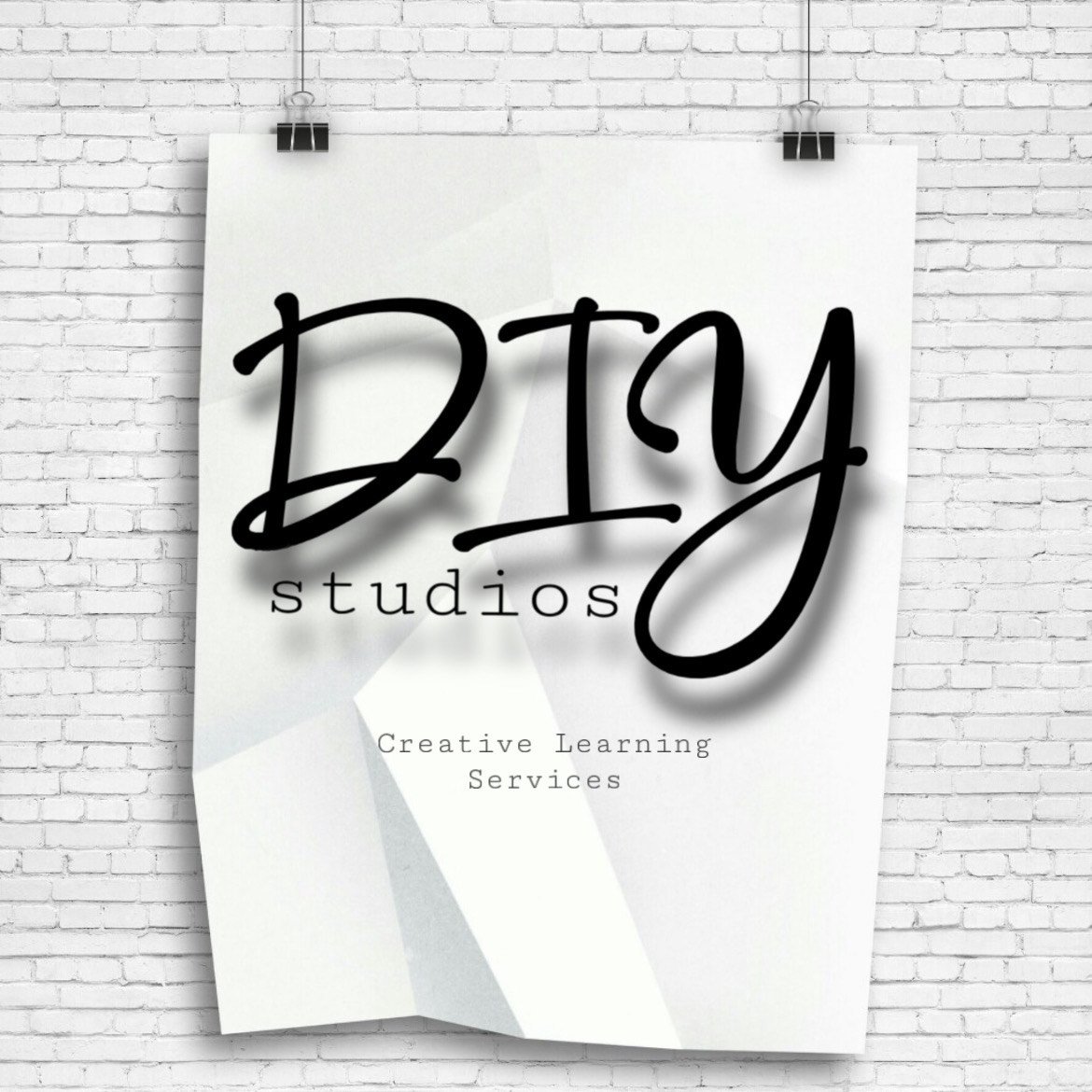 Logo Sign reading 'DIY Studios' with the text 'Creative Learning Services' underneath, hanging on a white brick wall.