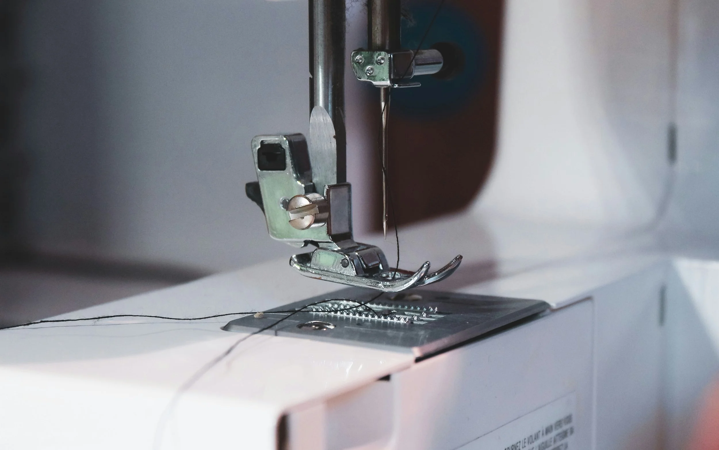 Close-up of a sewing machine needle, presser foot, and fabric, with the machine's interior mechanisms visible.