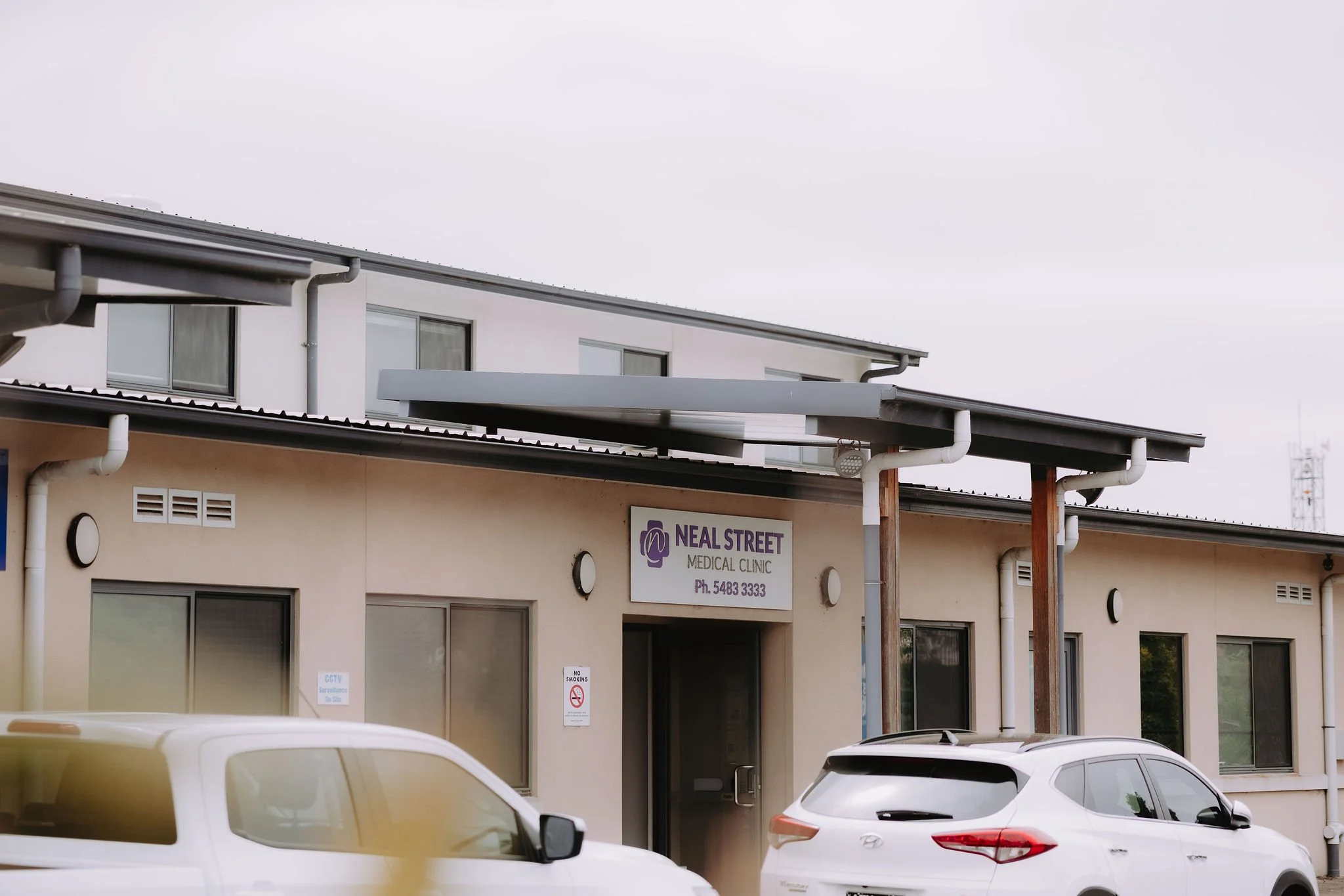 Exterior view of Neal Street Medical Clinic with parking lot and two cars parked in front, cloudy sky overhead.