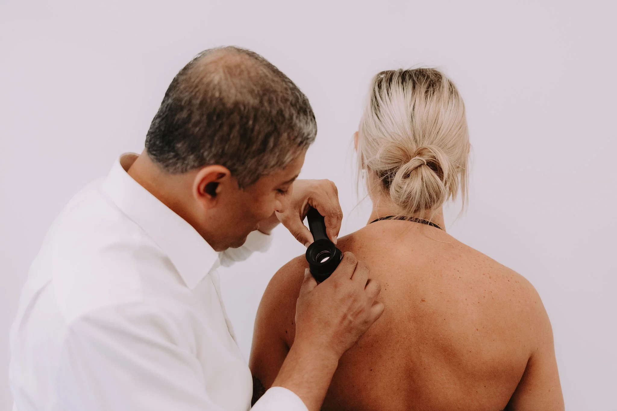 A doctor examining a woman's back with a magnifying glass in a clinical setting.