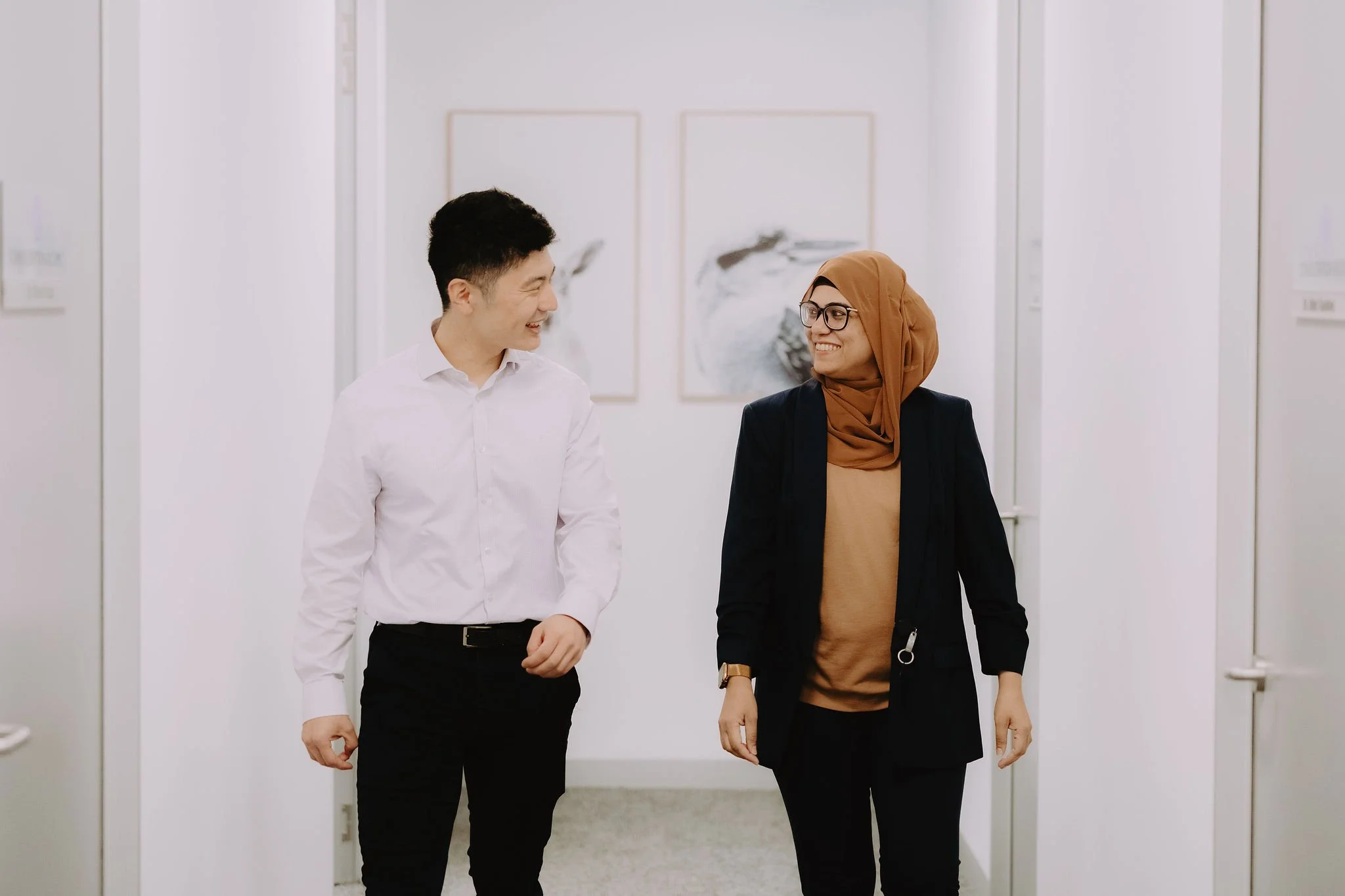 A man and a woman in a hallway, smiling and talking to each other.