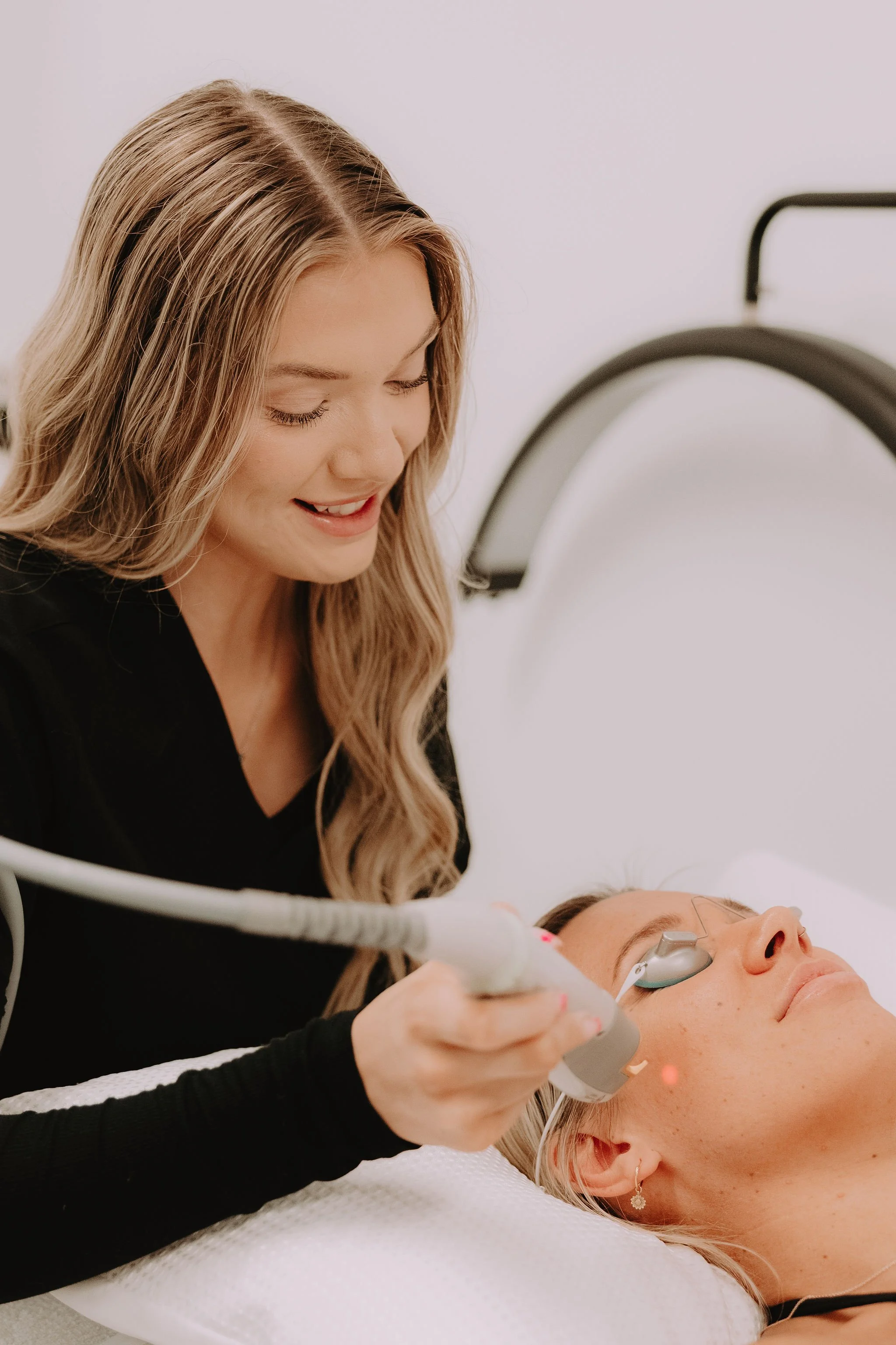 A woman receiving laser skin treatment from a technician in a medical spa setting.
