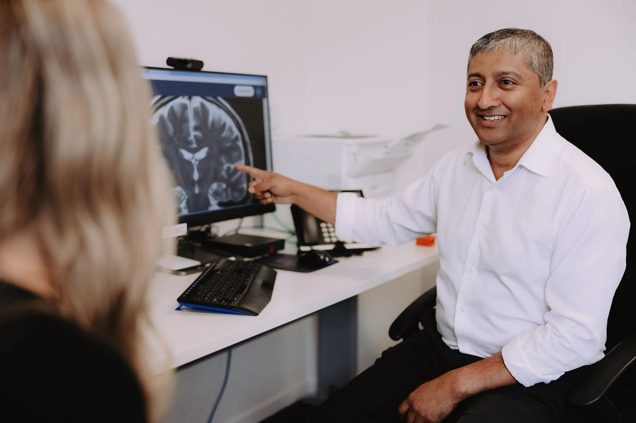 Doctor shows brain scan on computer monitor to patient in medical office.