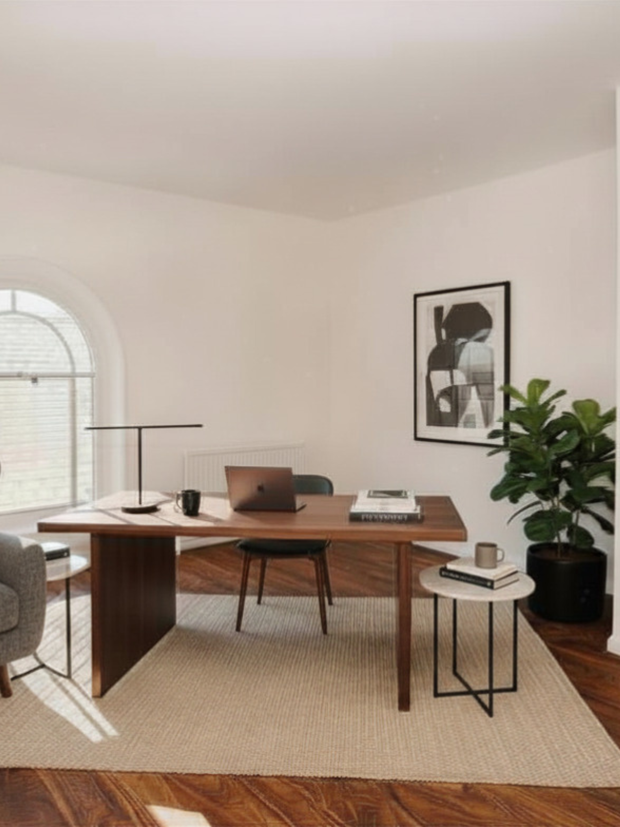 Modern home office with wooden desk, laptop, black mug, books, gray armchair, large window, potted plant, black and white abstract art, beige rug, wooden floor.