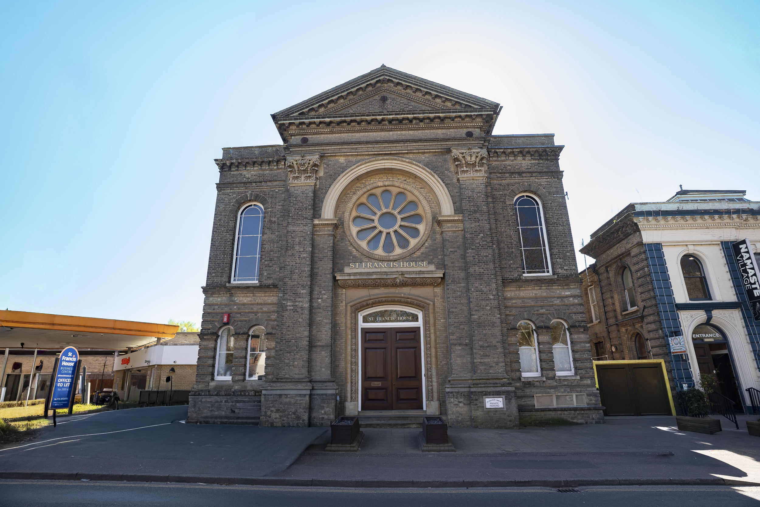 Image of the historic St. Francis House, a brick building with arched windows and ornate architectural details, with a blue sky in the background.
