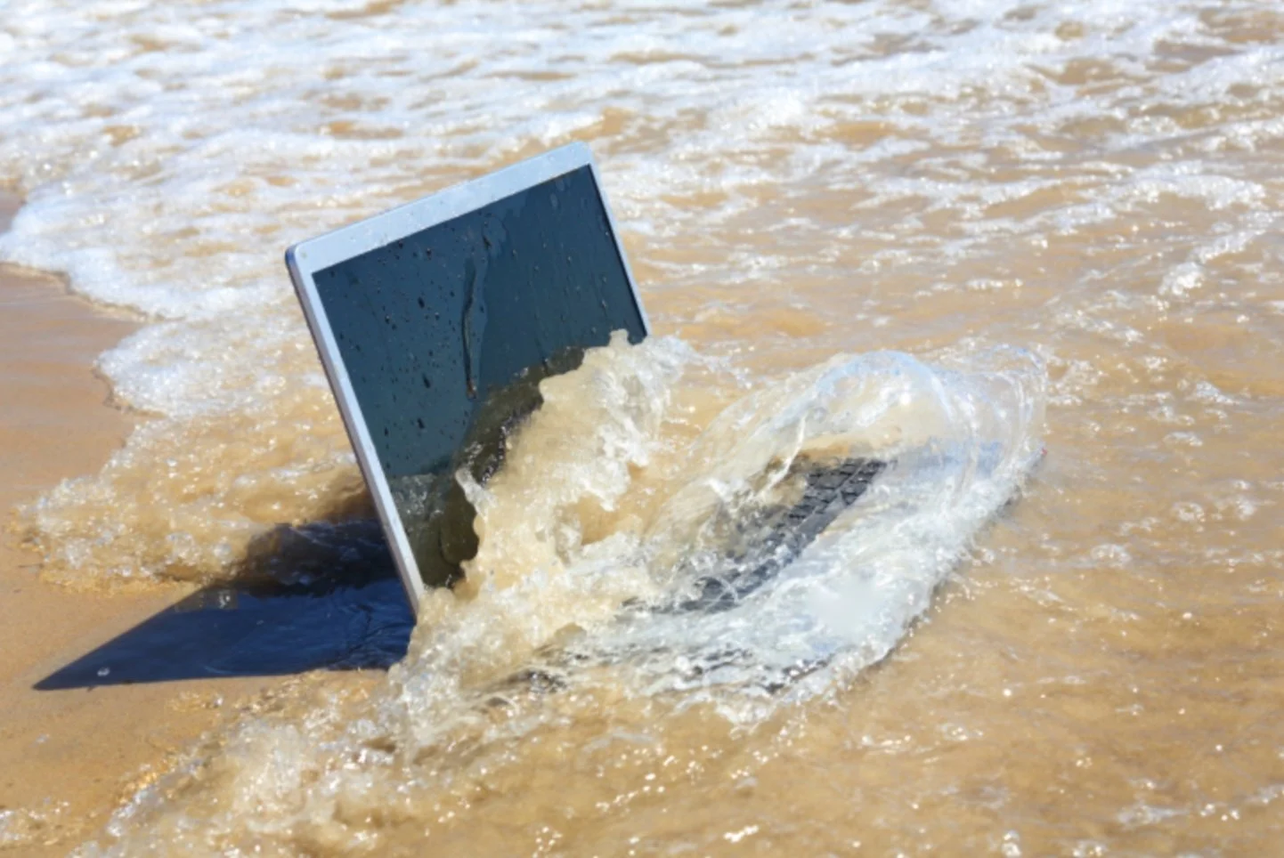 MacBook getting hit by a wave signifying that it is time to recycle it responsibly