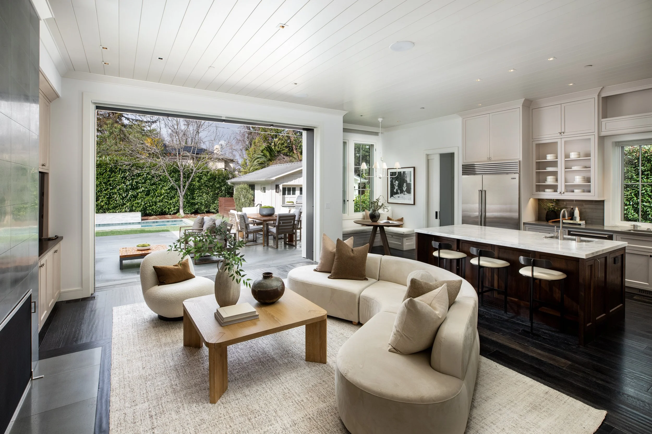 Modern open-plan living room and kitchen with large sliding glass door opening to a backyard patio with outdoor dining and seating area.